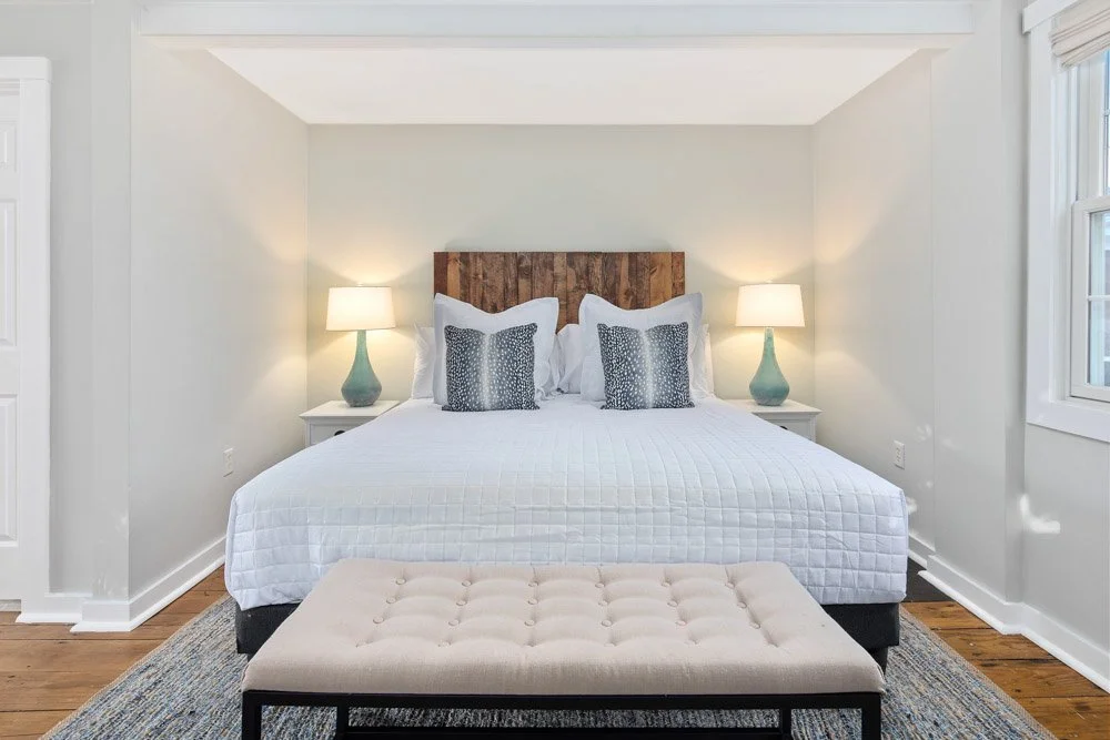 A bedroom with a large bed, two nightstands with lamps, and a beige tufted bench at the foot of the bed.