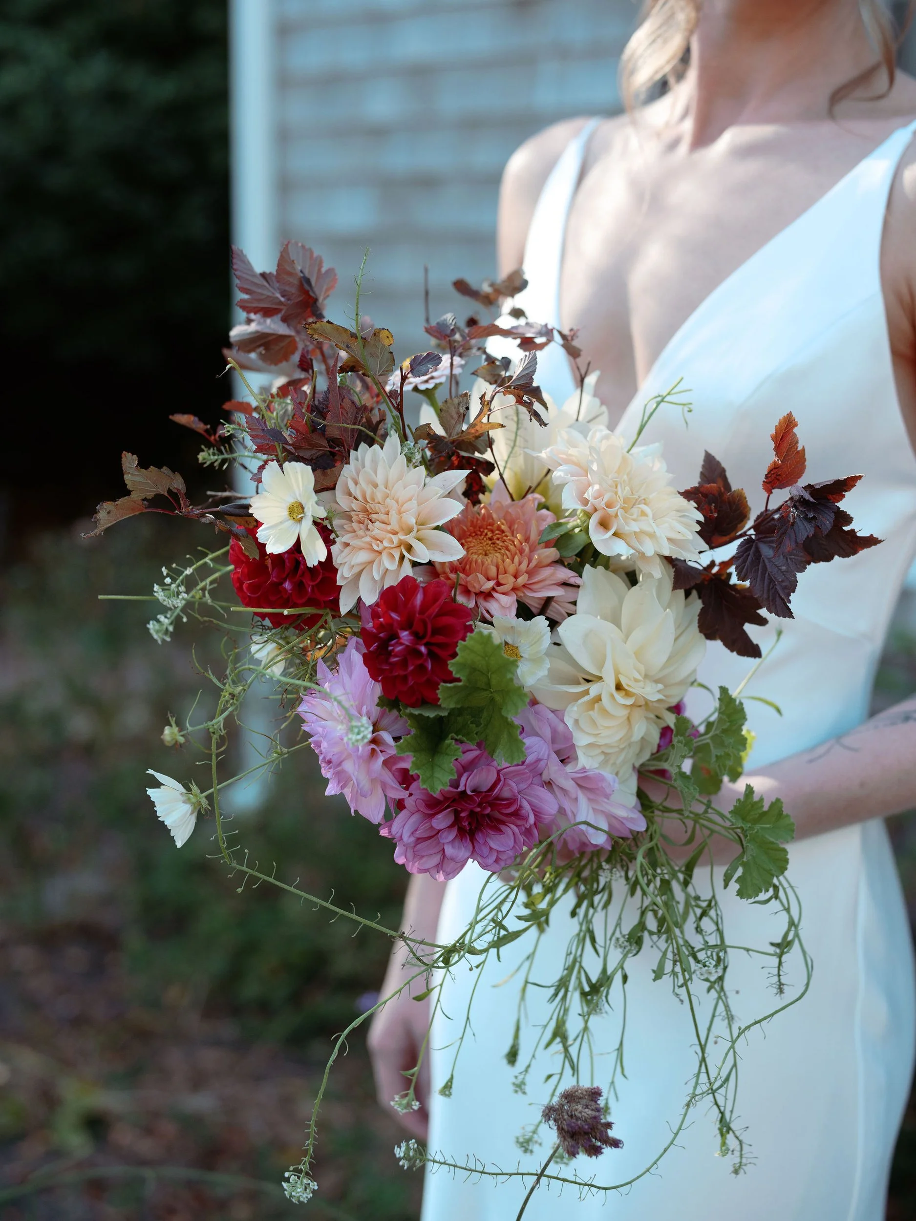 Woman in a white dress holding a colorful bouquet of flowers outdoors during a wedding at Lambert's Cove Inn on Martha's Vineyard.