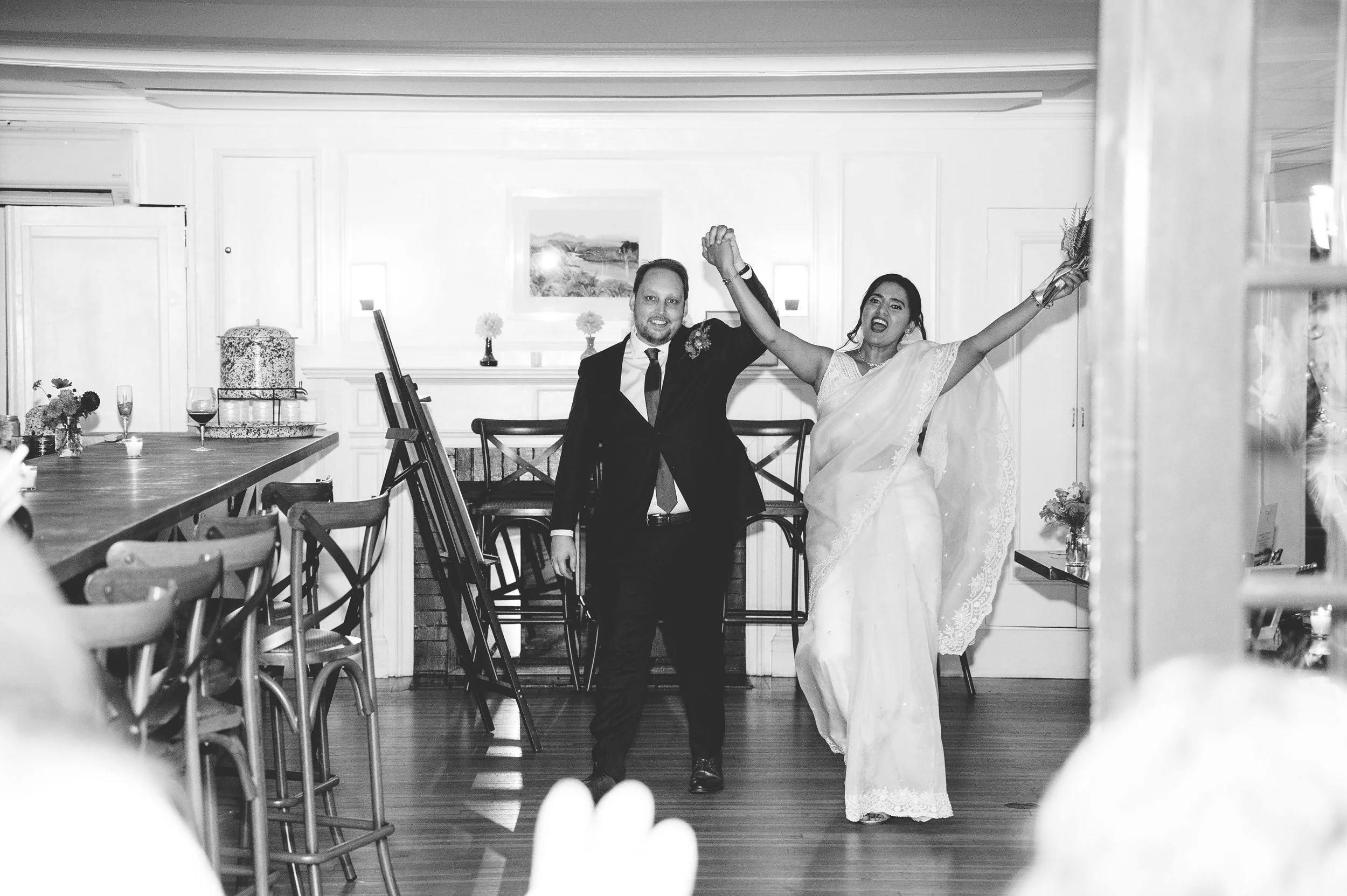 A black and white photo of a bride and groom dancing at their wedding reception at Lambert's Cove Inn on Martha's Vineyard in a decorated indoor venue, with chairs and tables visible in the background.