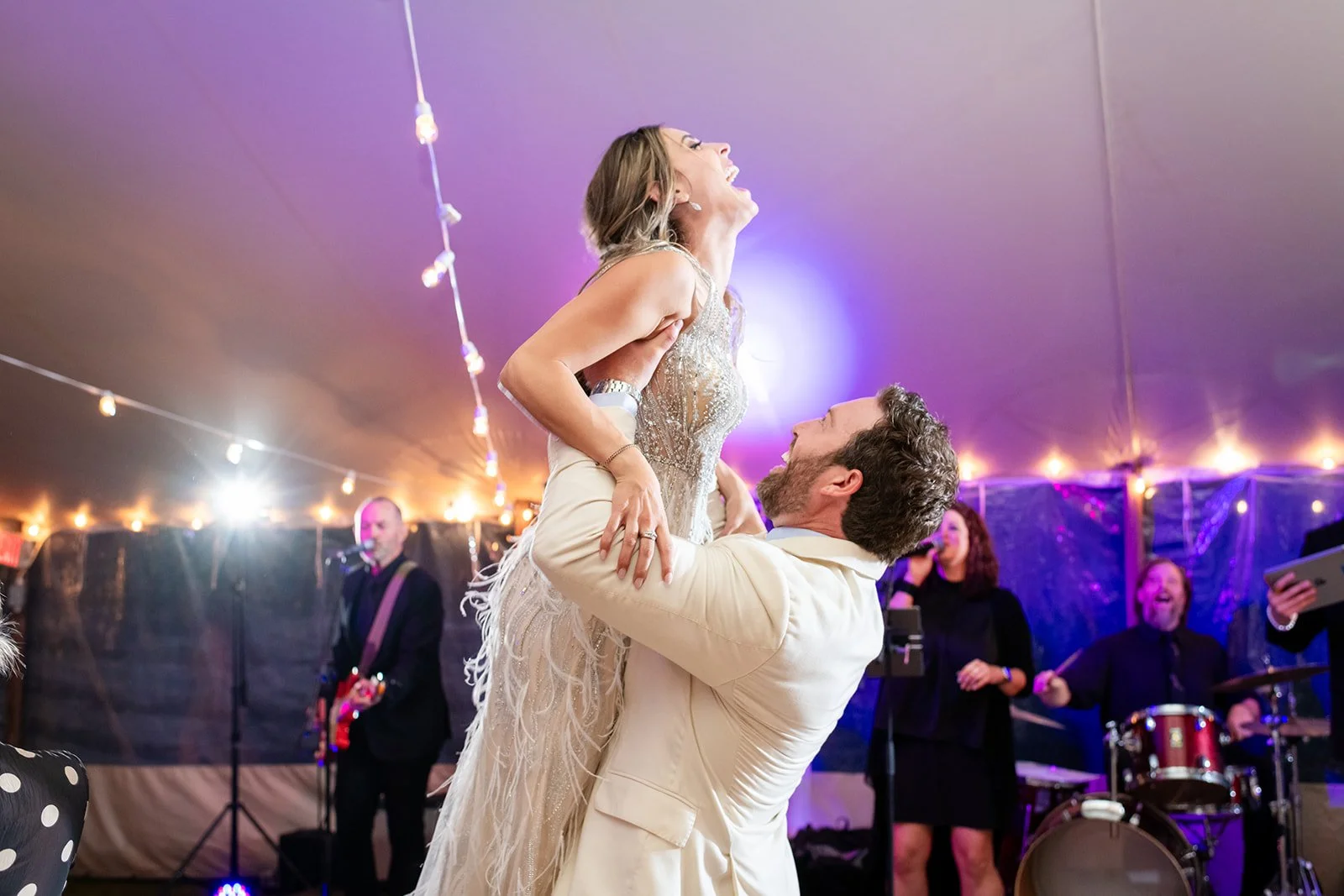 A couple dancing at their wedding reception at Lambert's Cove Inn on Martha's Vineyard surrounded by musicians and wedding guests under a decorated tent with string lights.