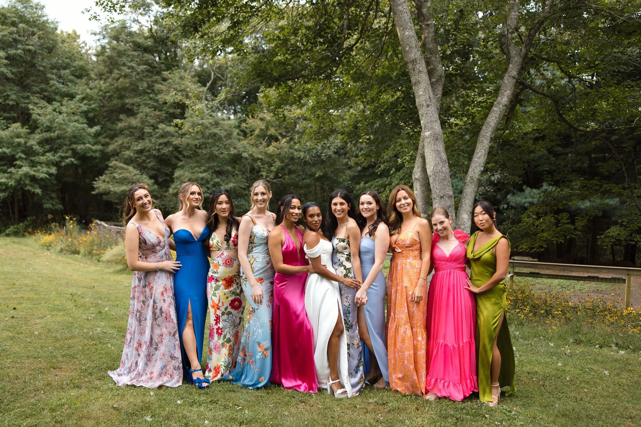 Group of women in colorful dresses standing outdoors in a park on a cloudy day before a wedding at Lambert's Cove Inn on Martha's Vineyard.