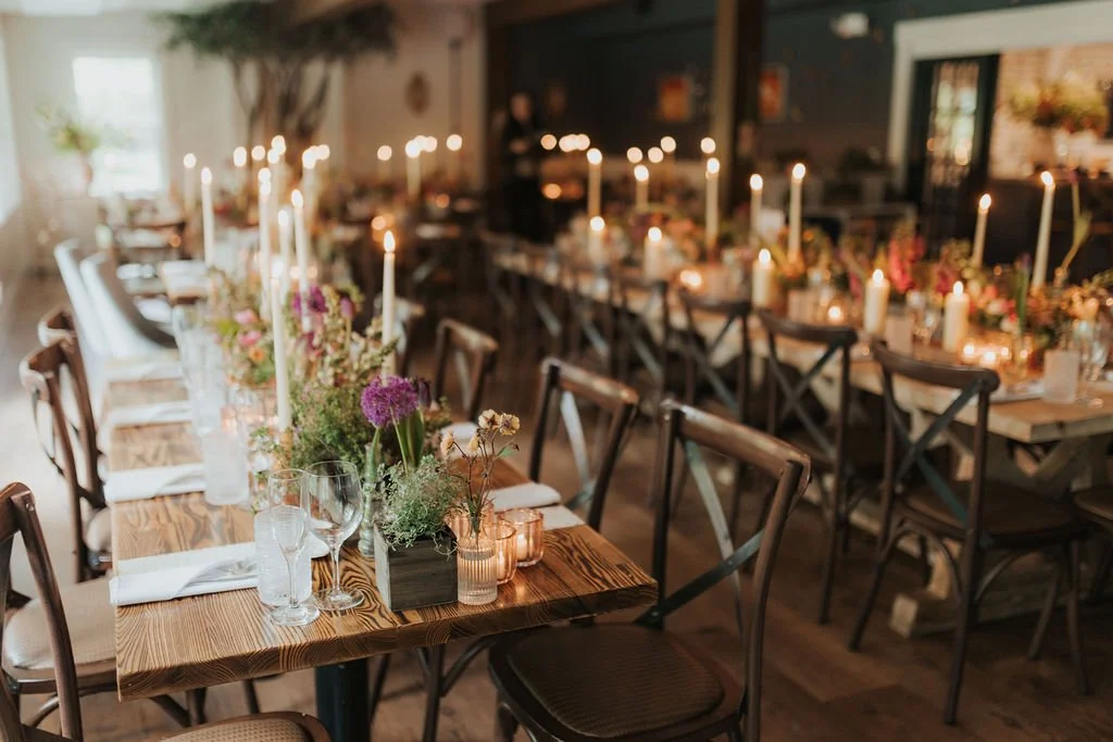 A beautifully set dining table in a cozy restaurant with candles, floral centerpieces, wine glasses, and neatly folded napkins, ready for a meal.