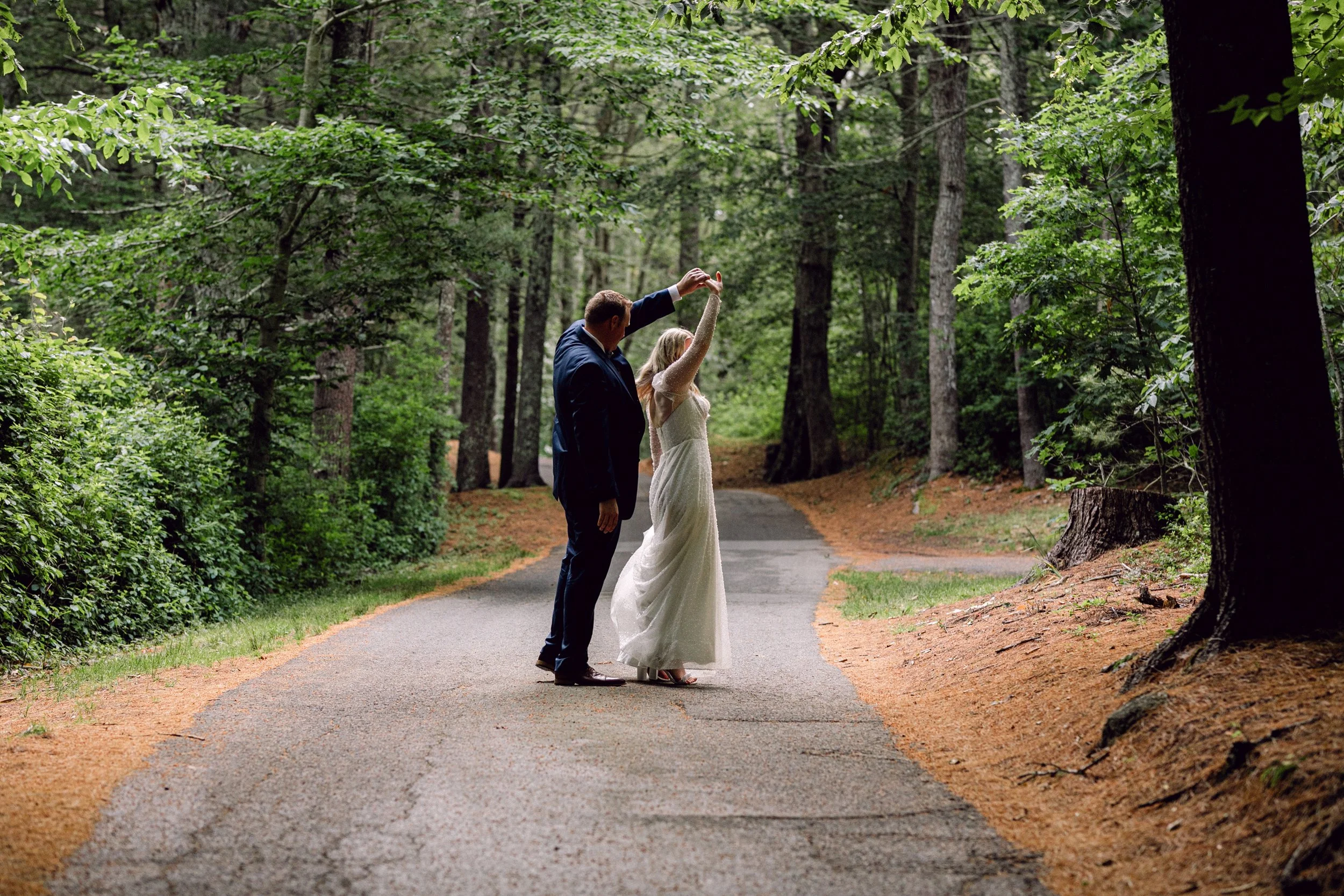 A bride and groom dancing on a forested path surrounded by green trees at Lambert's Cove Inn on Martha's Vineyard.
