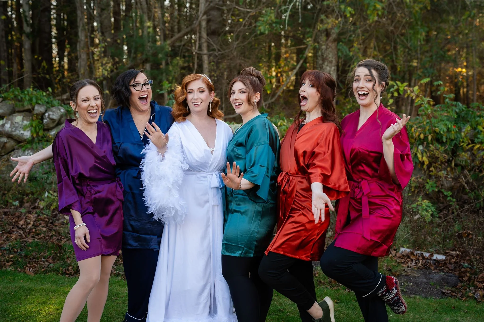 Six women in colorful satin robes celebrating outdoors on a fall day with trees in the background at Lambert's Cove Inn on Martha's Vineyard.