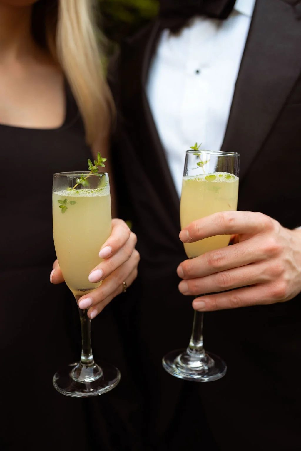 Two people holding champagne flutes filled with a light yellow beverage garnished with small green herbs at Lambert's Cove Inn on Martha's Vineyard.