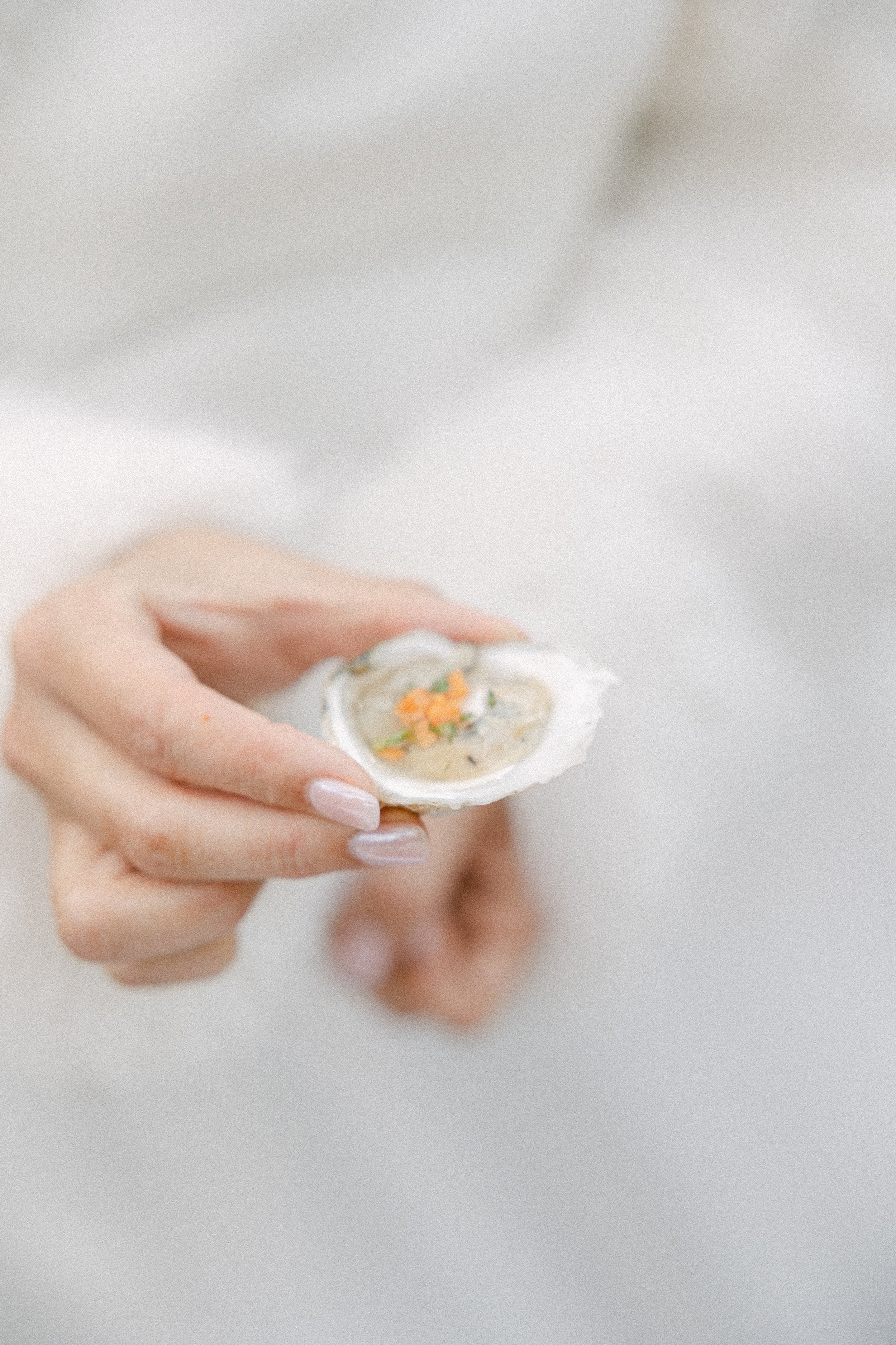 A hand with well-manicured nails holding an oyster shell with a small oyster inside, filled with ingredients. The food was prepared by the catering team at Lambert's Cove Inn on Martha's Vineyard. 