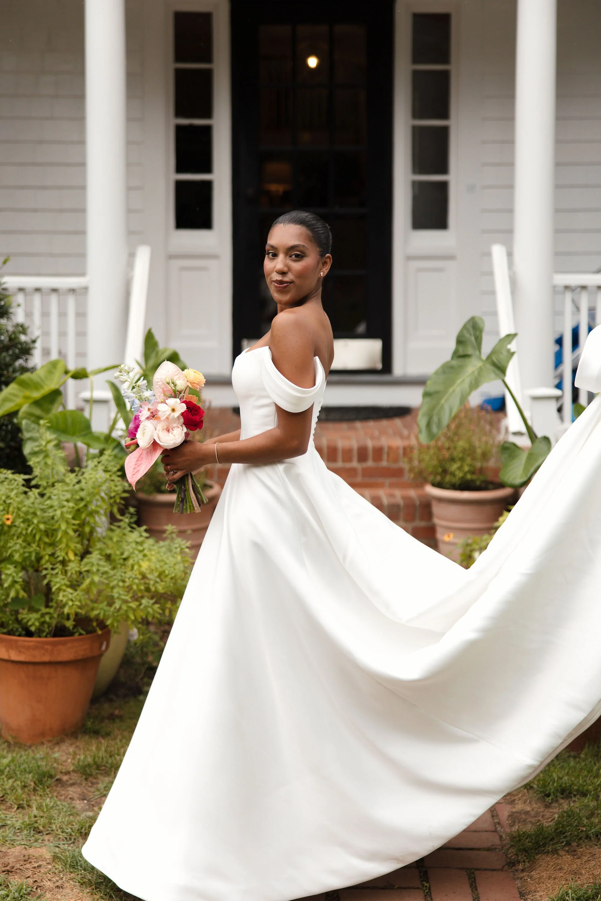 A woman in a wedding dress standing outside a house holding a bouquet of flowers before a wedding ceremony at Lambert's Cove Inn on Martha's Vineyard.