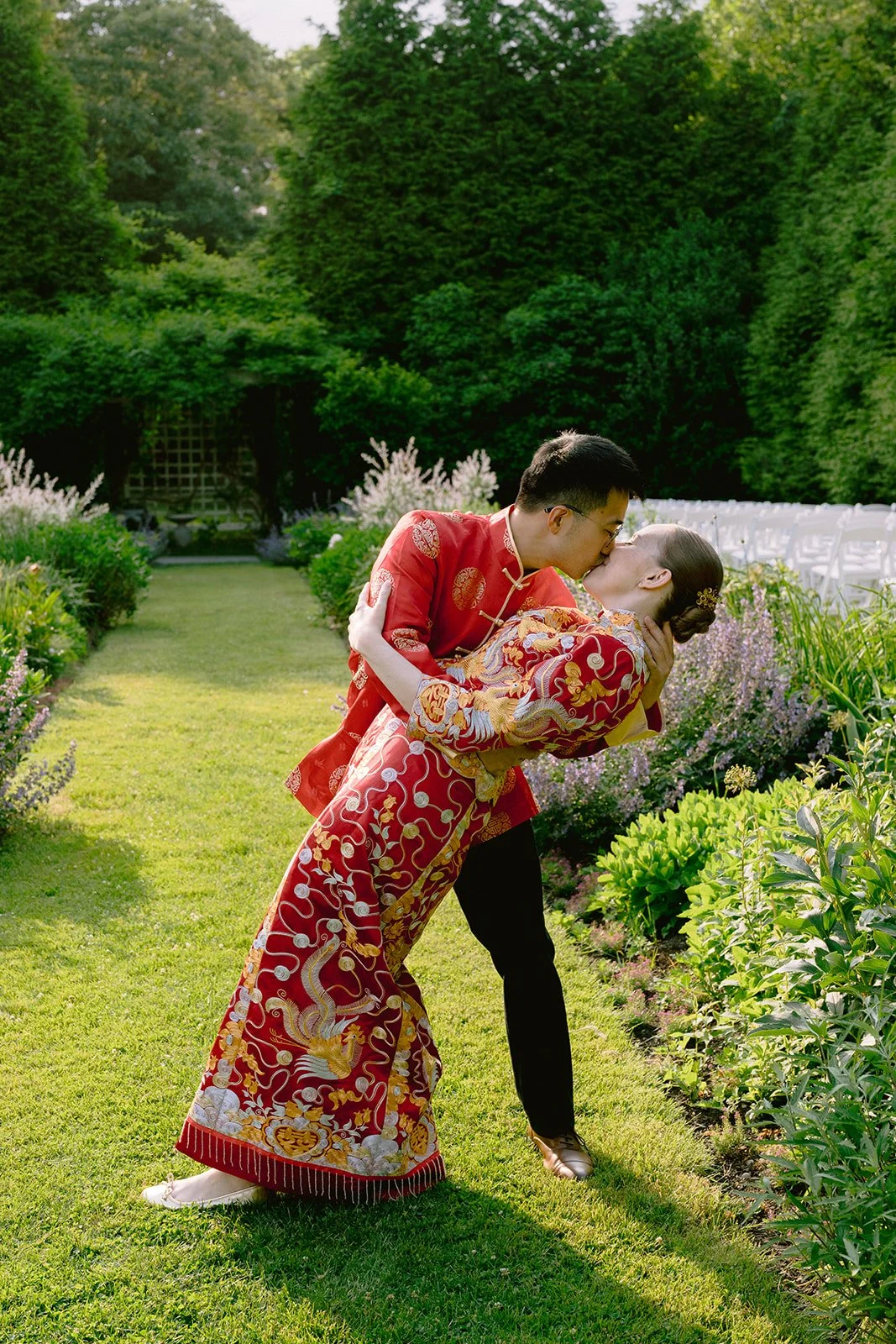Couple in traditional Chinese wedding attire sharing a kiss in a lush garden during a wedding at Lambert's Cove Inn on Martha's Vineyard.