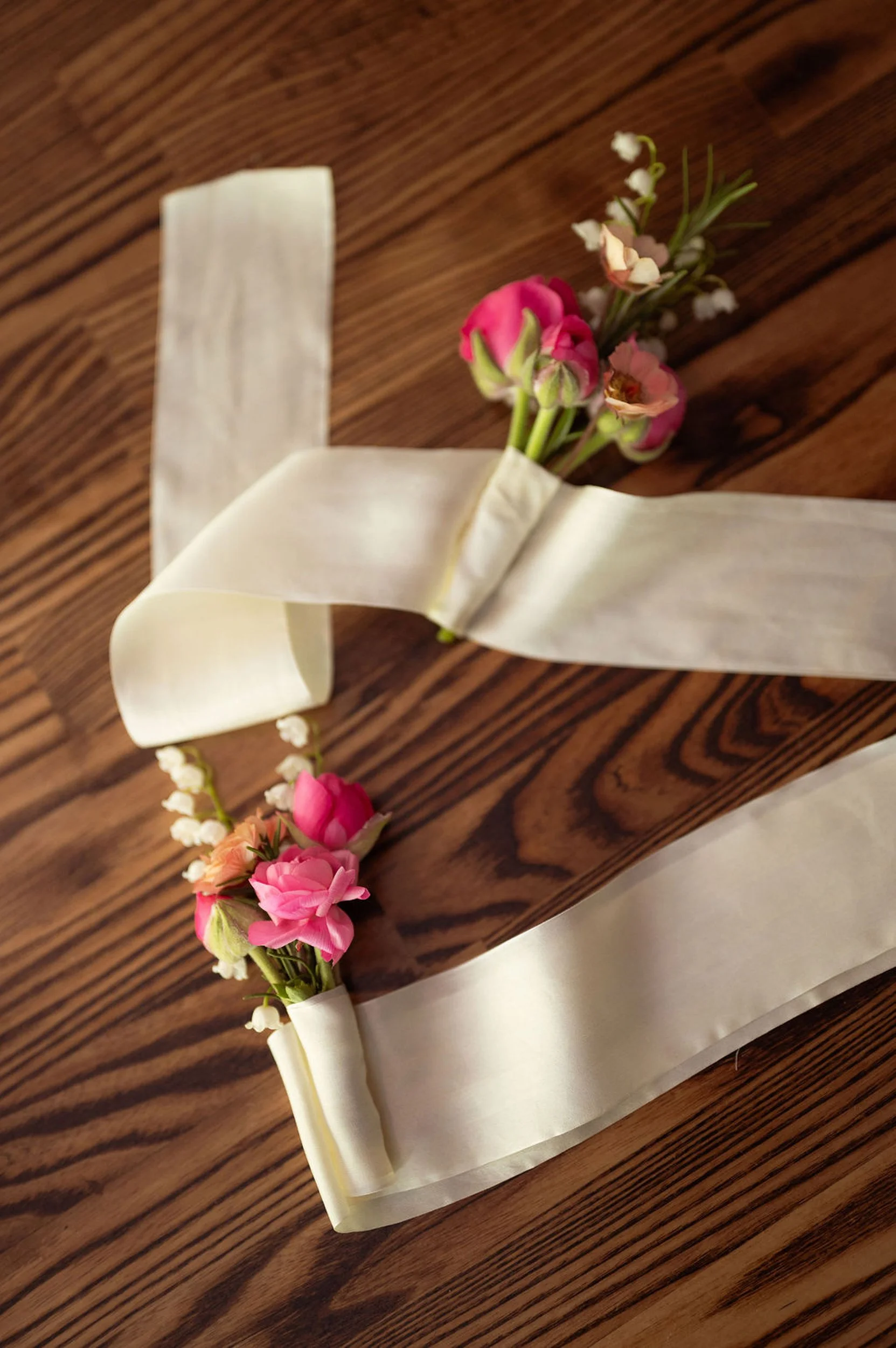 A floral corsage with pink and white flowers wrapped in white satin ribbon on a wooden surface. The flowers were custom grown for a wedding at Lambert's Cove Inn on Martha's Vineyard.