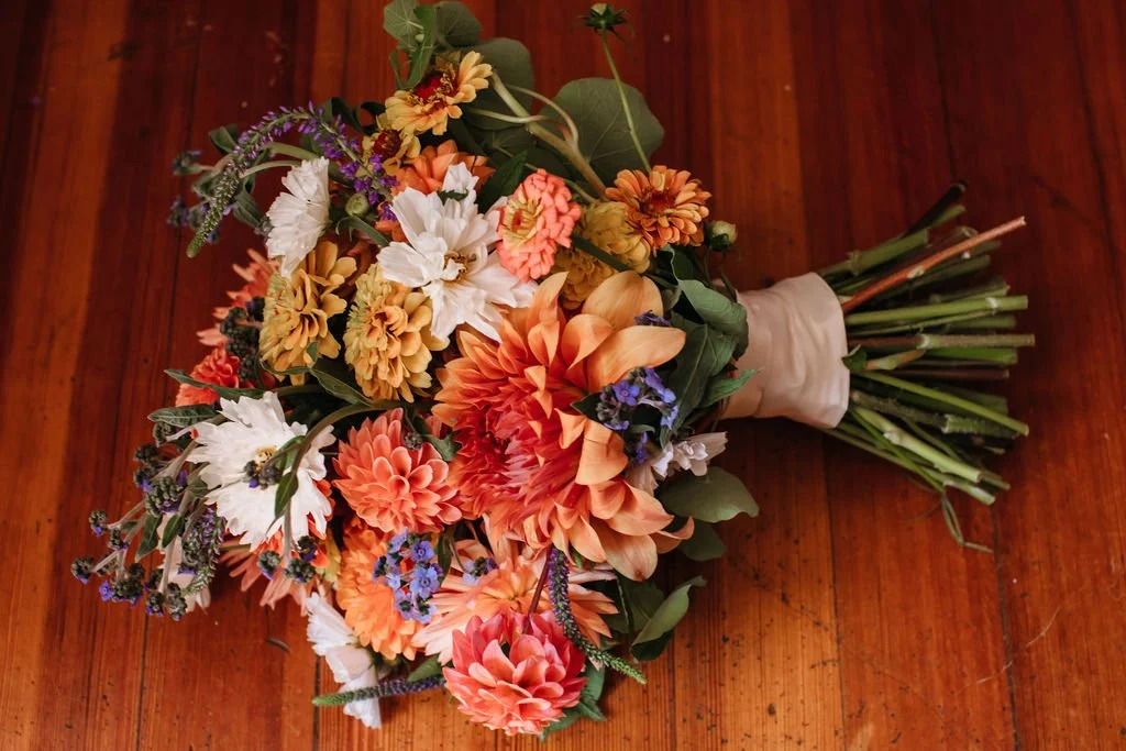 Bouquet of orange, white, and purple flowers on a wooden surface. The flowers were custom grown and designed by Bridget Sampson at Lambert's Cove Inn on Martha's Vineyard.