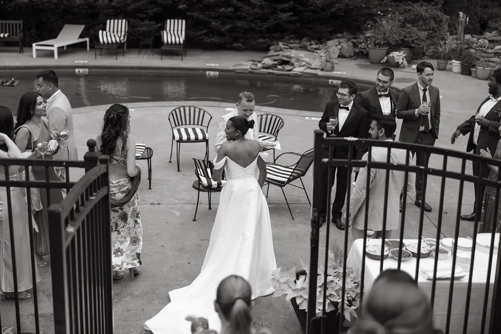 Black and white photo of a wedding reception at Lambert's Cove Inn on Martha's Vineyard gathering near a swimming pool, with guests socializing and a bride in a white dress facing away from the camera.