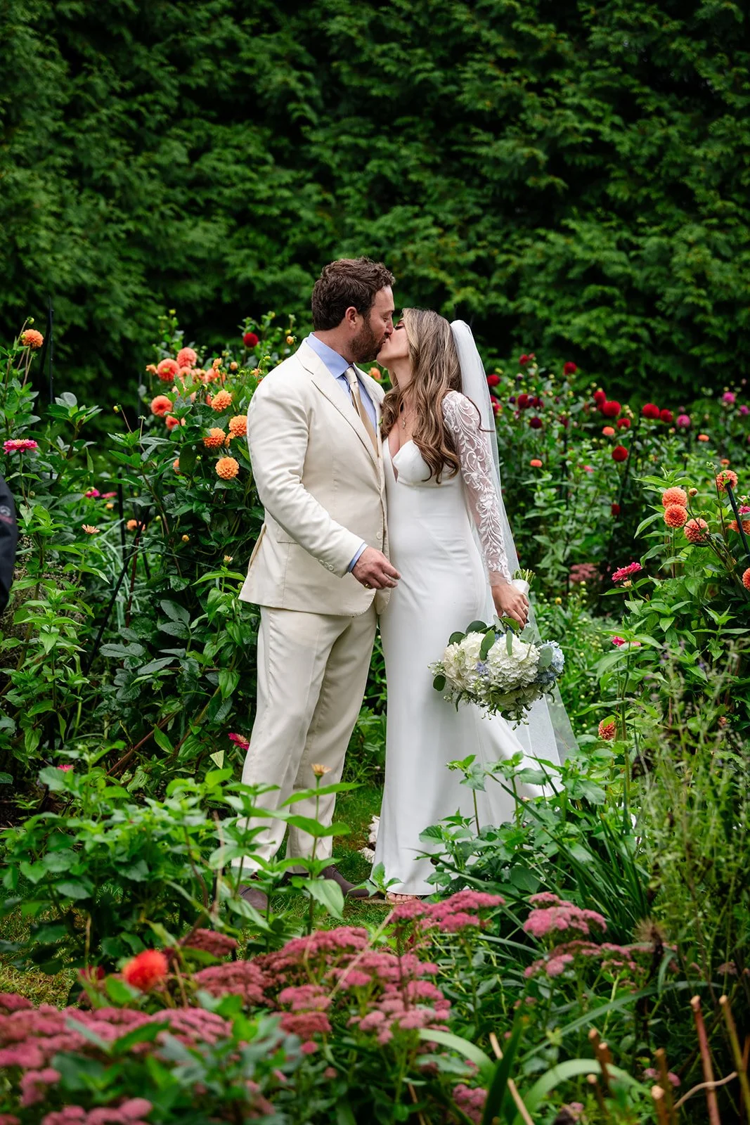 A bride and groom sharing a kiss in a lush garden with colorful flowers at Lambert's Cove Inn on Martha's Vineyard.