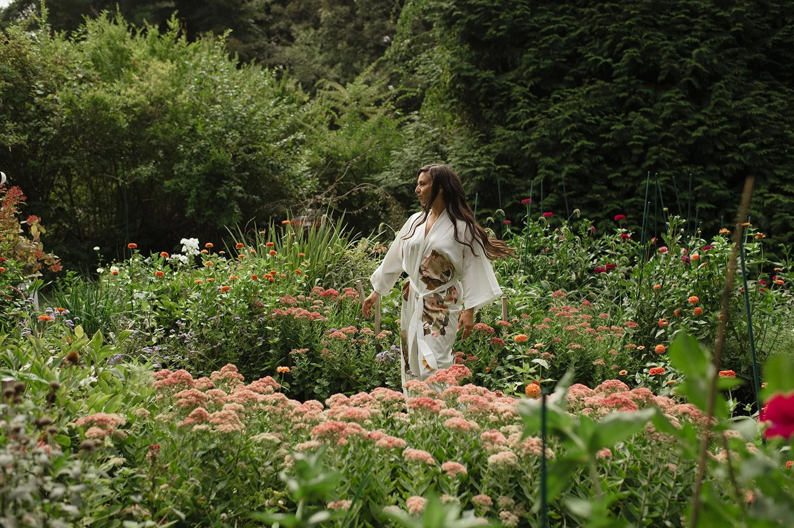 A woman in a white floral kimono walking through a lush, green garden at Lambert's Cove Inn on Martha's Vineyard filled with colorful flowers.