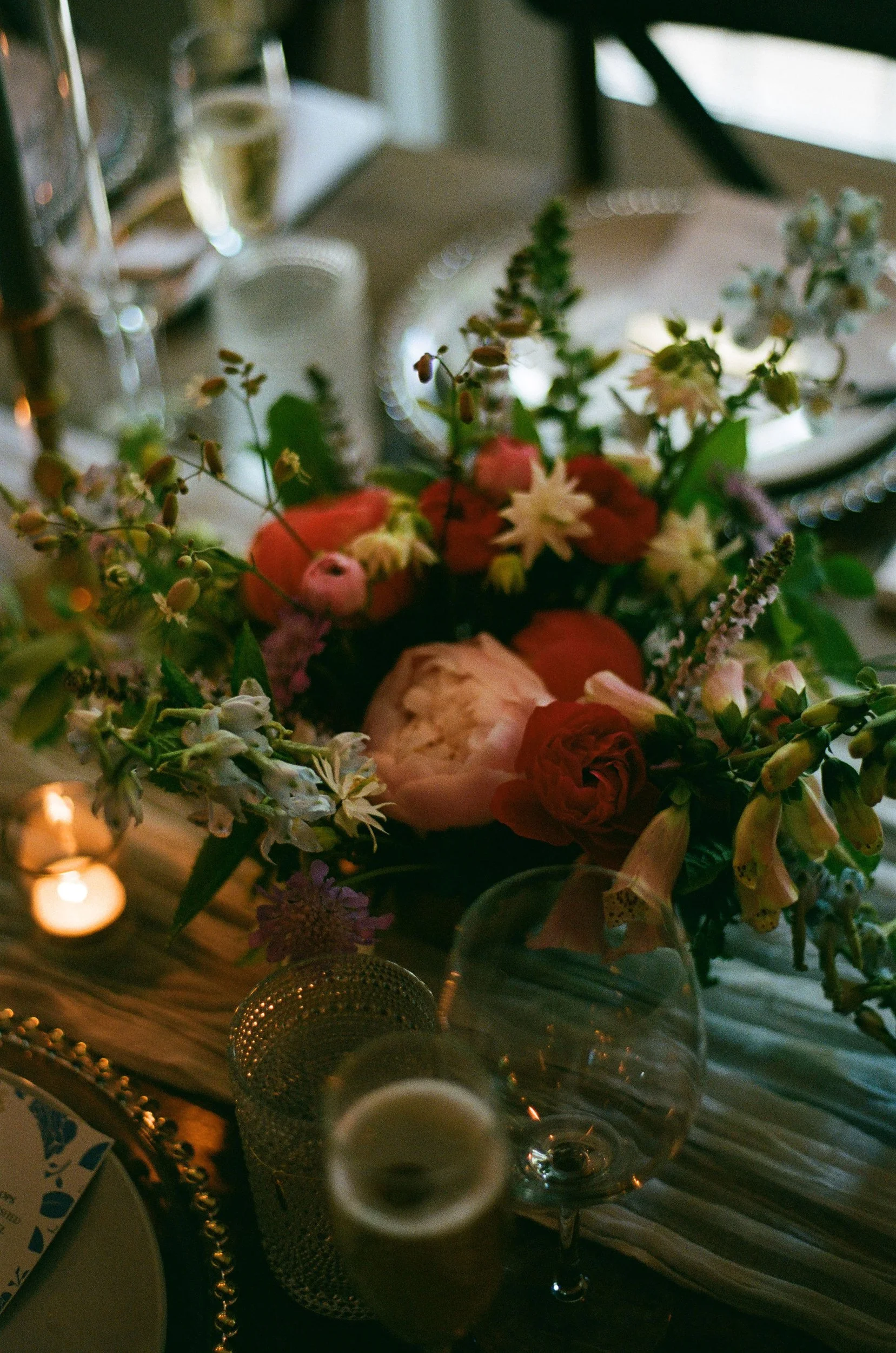 A table setting with a bouquet of mixed flowers, wine glasses, and candles with warm lighting at Lambert's Cove Inn on Martha's Vineyard.