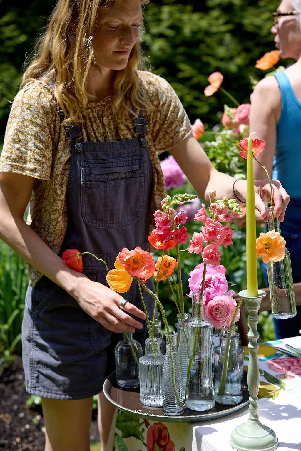 A woman arranging flowers in glass vases outdoors during daytime, with others nearby, surrounded by greenery before a wedding at Lambert's Cove Inn on Martha's Vineyard.