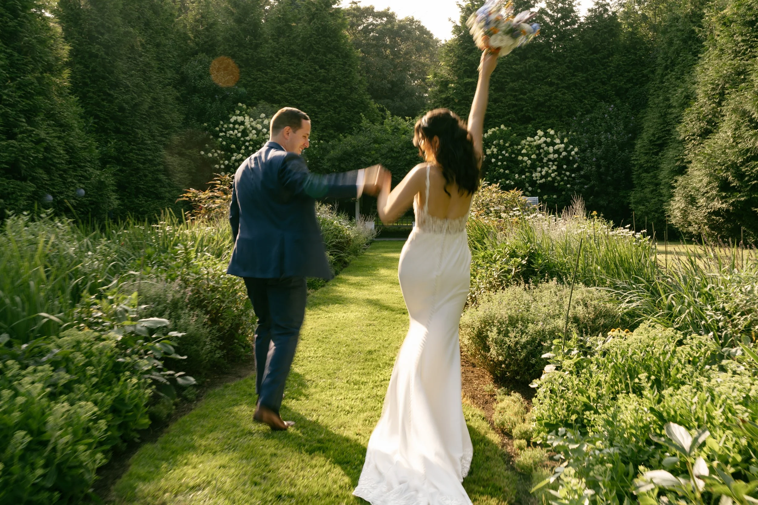 A bride and groom dancing in a lush garden during a wedding celebration, sunlight filtering through the trees.