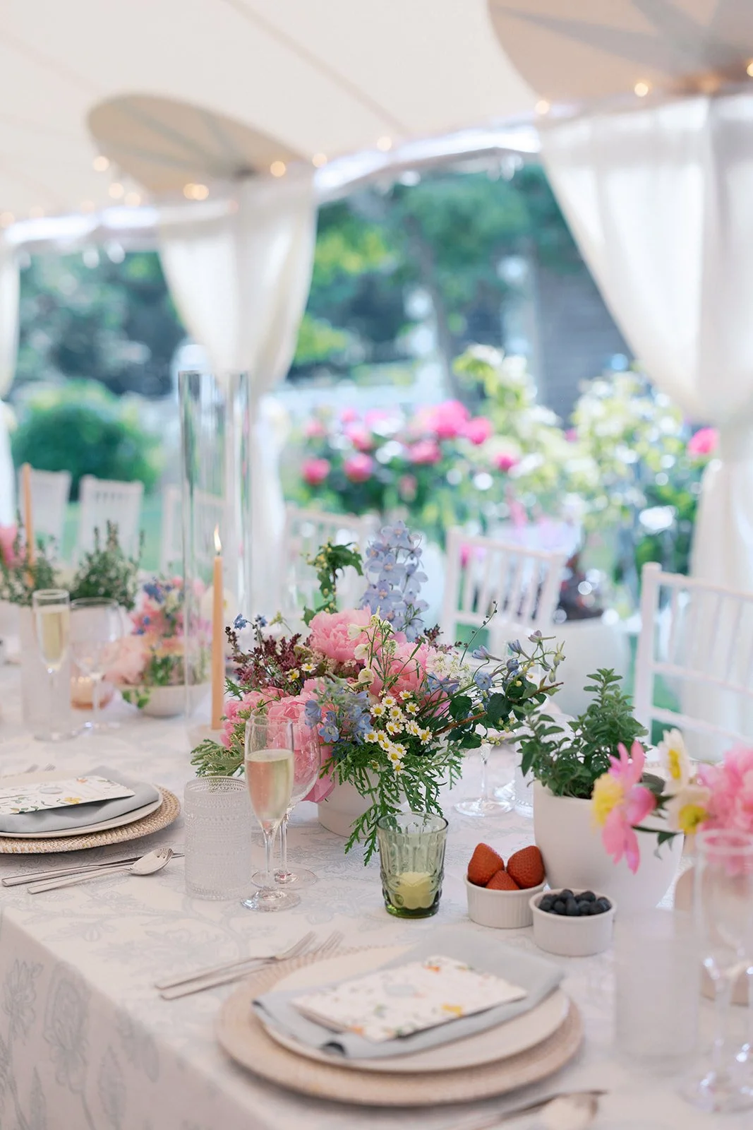 Table decorated with pink and purple flowers, candles, champagne glasses, and neatly set plates and utensils, under a tent  at Lambert's Cove Inn on Martha's Vineyard.