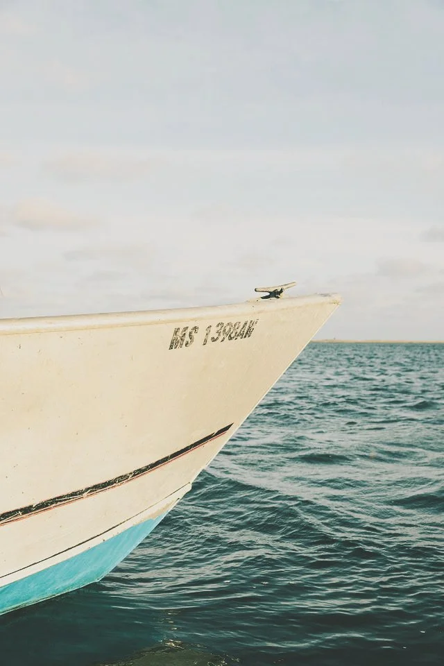 Close-up of the bow of a boat on the water, with a small aircraft model on its edge and a partly cloudy sky in the background.