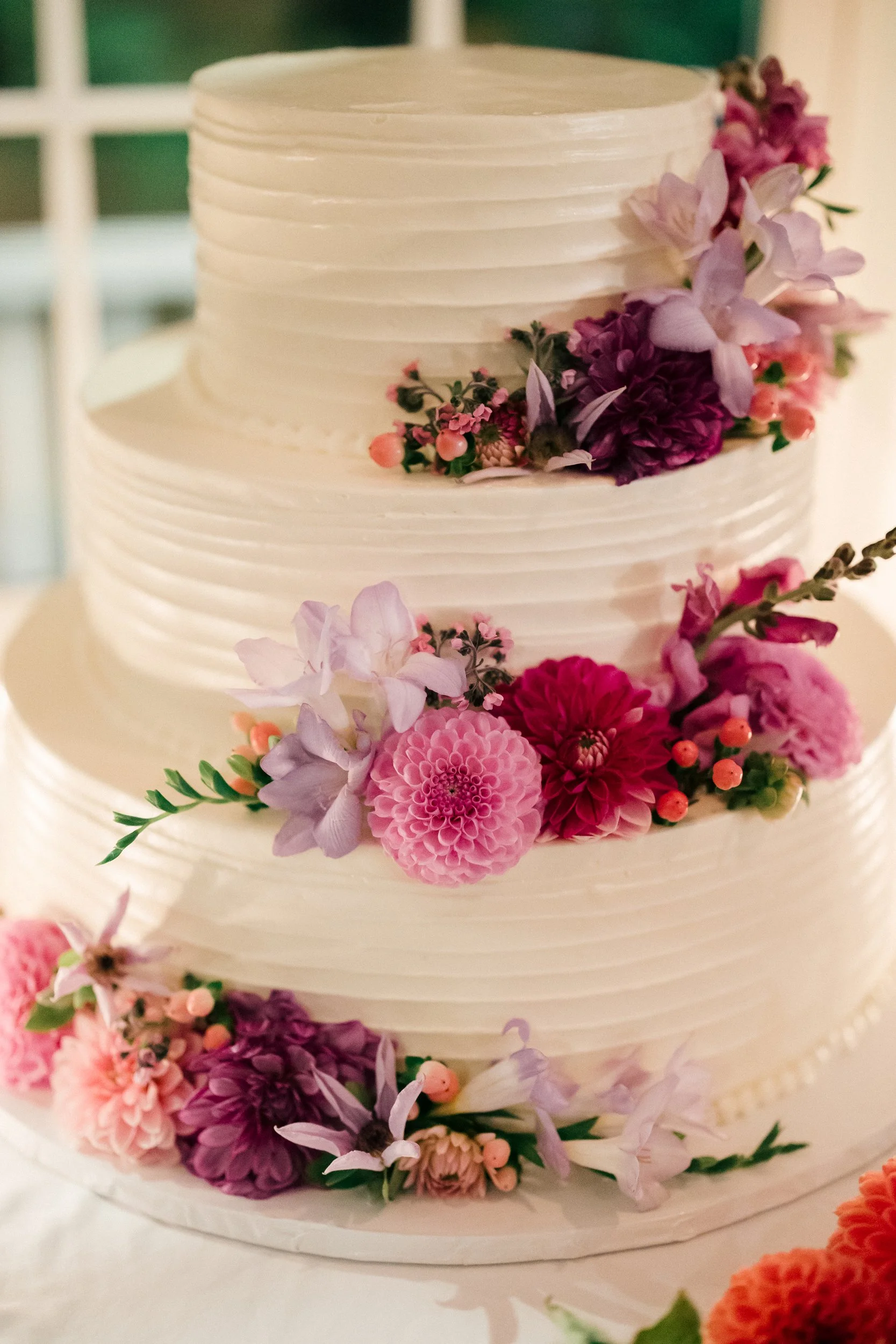 Close-up of a multi-tiered white wedding cake decorated with pink, purple, and peach flowers and green leaves, during a wedding reception at Lambert's Cove Inn on Martha's Vineyard.