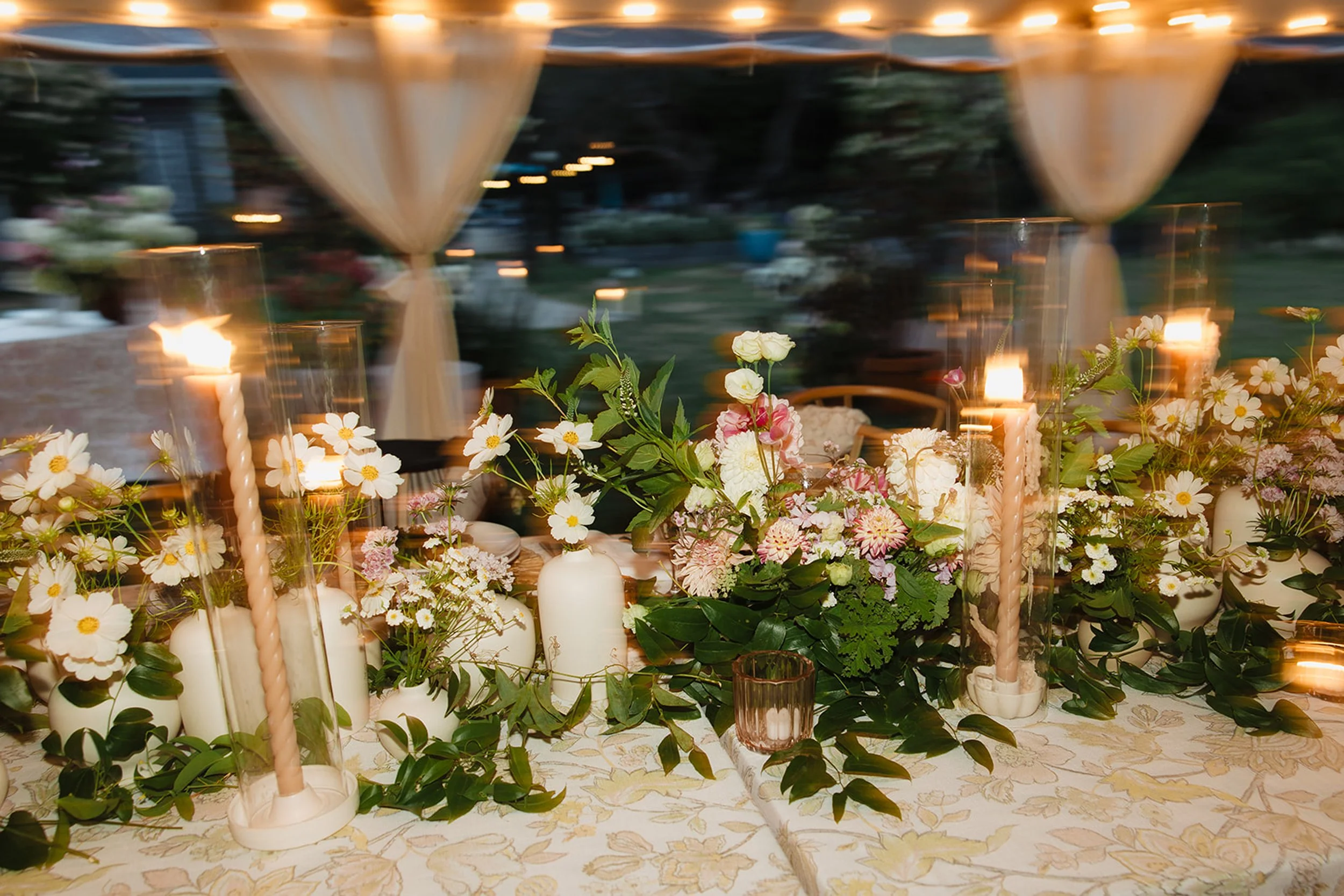 A floral centerpiece with white, pink, and green flowers on a table, illuminated by candles in a dimly lit room with a decorated ceiling at Lambert's Cove Inn on Martha's Vineyard.
