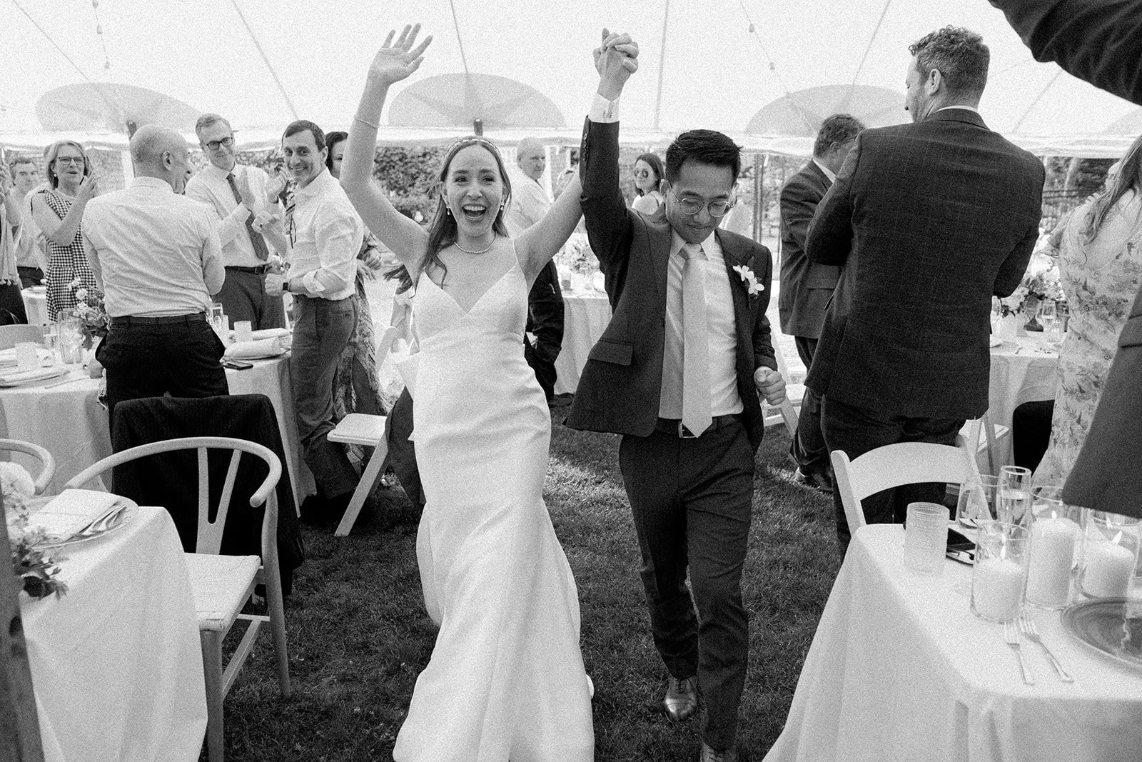 A bride and groom celebrating during their wedding at Lambert's Cove Inn on Martha's Vineyard, holding hands in the air and smiling.