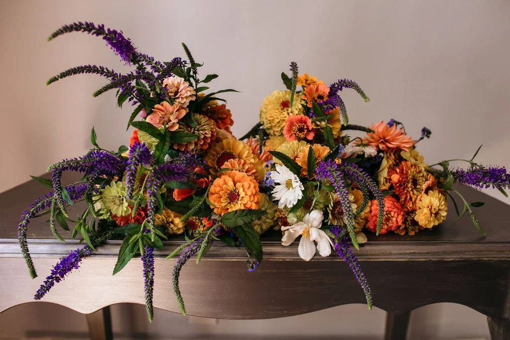 Colorful flower arrangement with orange, yellow, white, and purple flowers on a dark wooden table at Lambert's Cove Inn on Martha's Vineyard.
