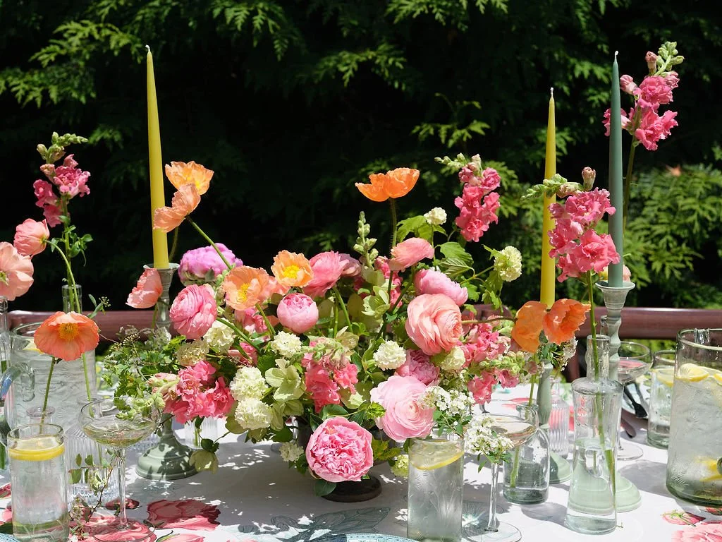 A table decorated with pink, peach, and white flowers, with tall candles in glass holders, set outdoors before a wedding at Lambert's Cove Inn on Martha's Vineyard.