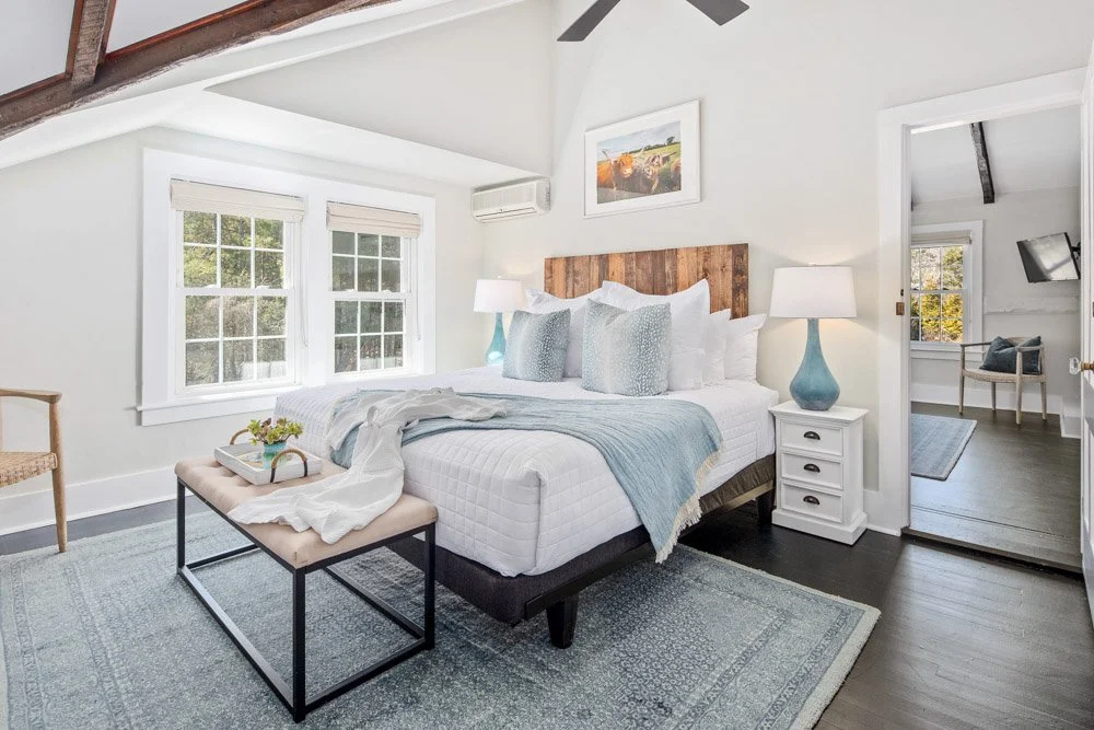 Clean, cozy bedroom at Lambert's Cove Inn on Martha's Vineyard with white walls, wooden accents, large windows, and a neatly made bed with white and light blue bedding.