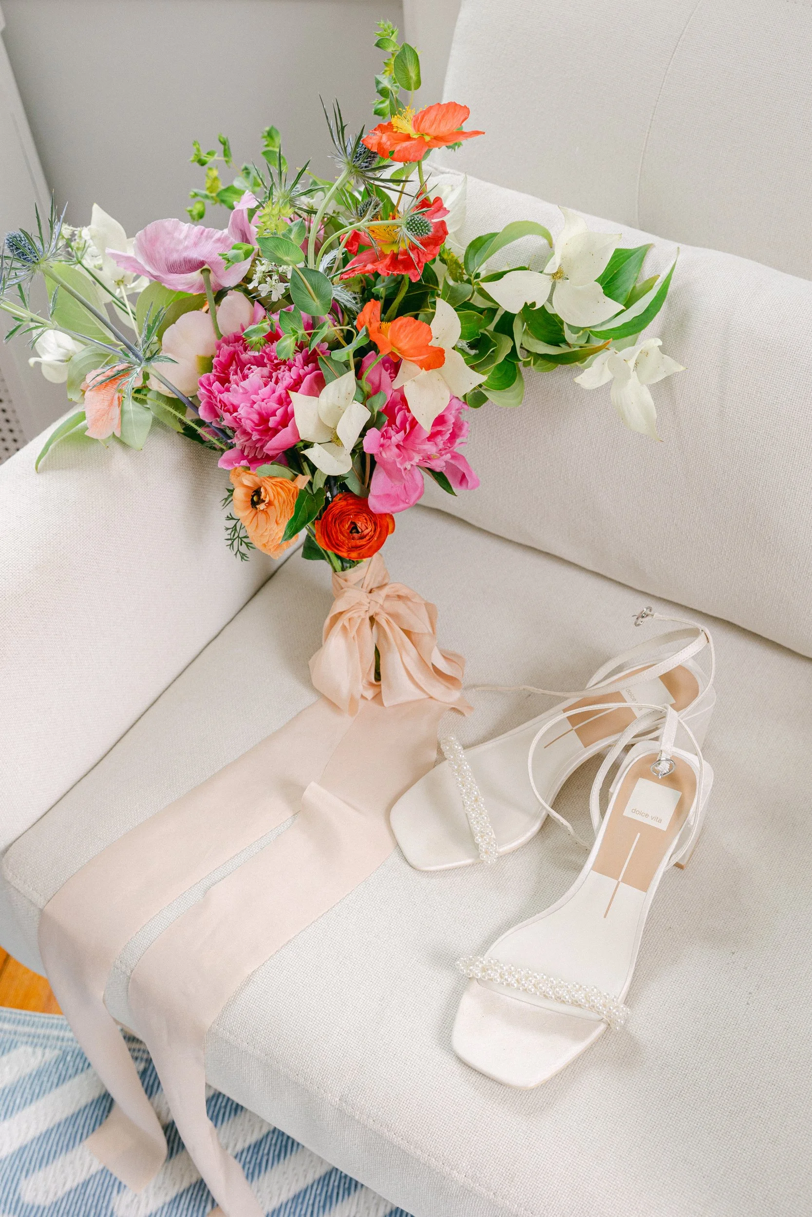 A bouquet of assorted flowers, including white, pink, orange, and red blooms with green foliage, resting on a white upholstered sofa during a wedding at Lambert's Cove Inn on Martha's Vineyard.