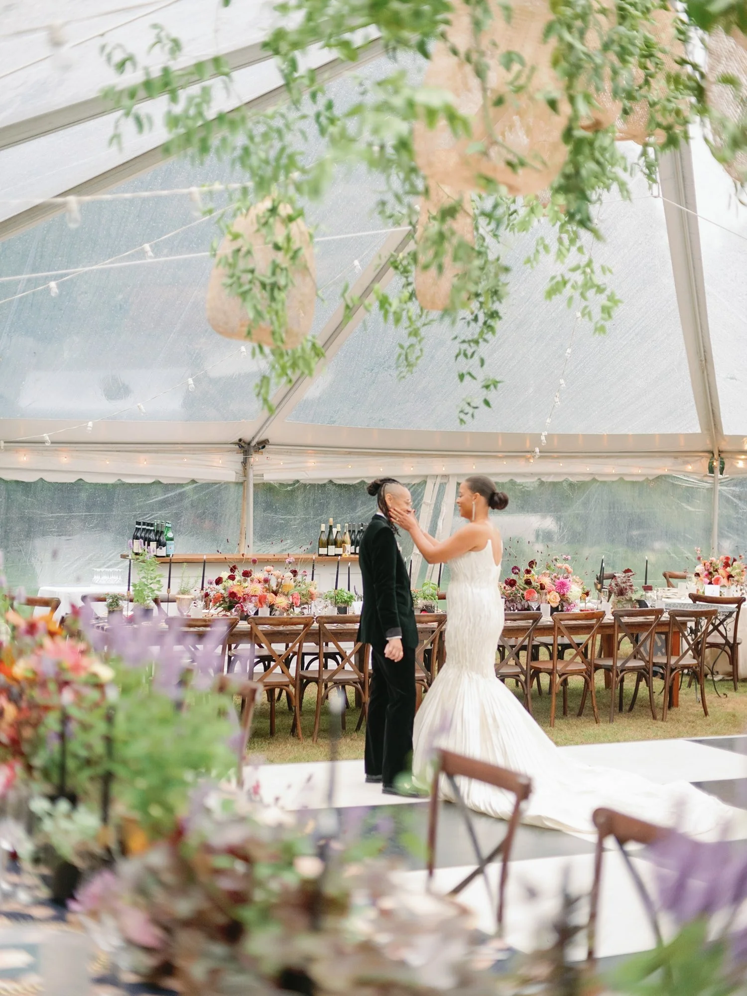 A bride and groom sharing a moment during their wedding reception in a decorated outdoor tent, with floral arrangements and string lights at Lambert's Cove Inn on Martha's Vineyard.