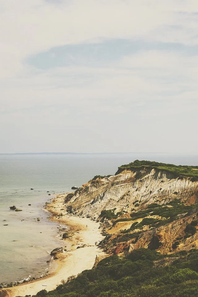 Coastal landscape with white cliffs, sandy beach, and ocean under cloudy sky.