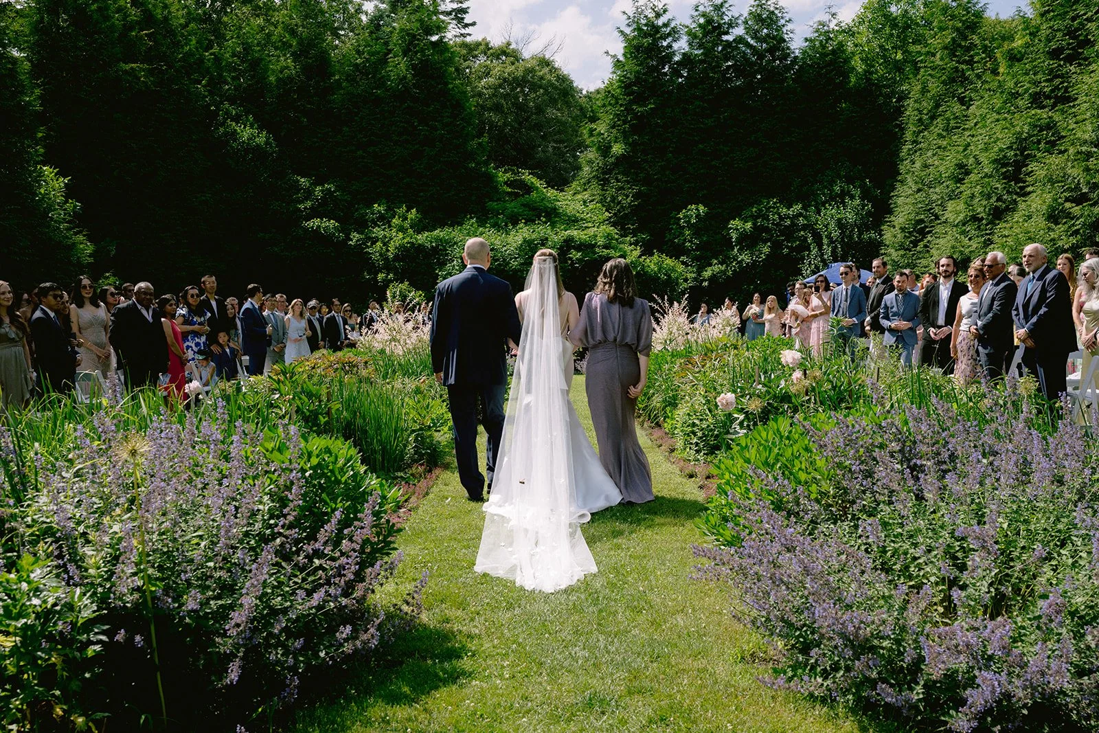 Wedding ceremony outdoors with bride and groom walking down the aisle, surrounded by guests and lush greenery, during a wedding at Lambert's Cove Inn on Martha's Vineyard.
