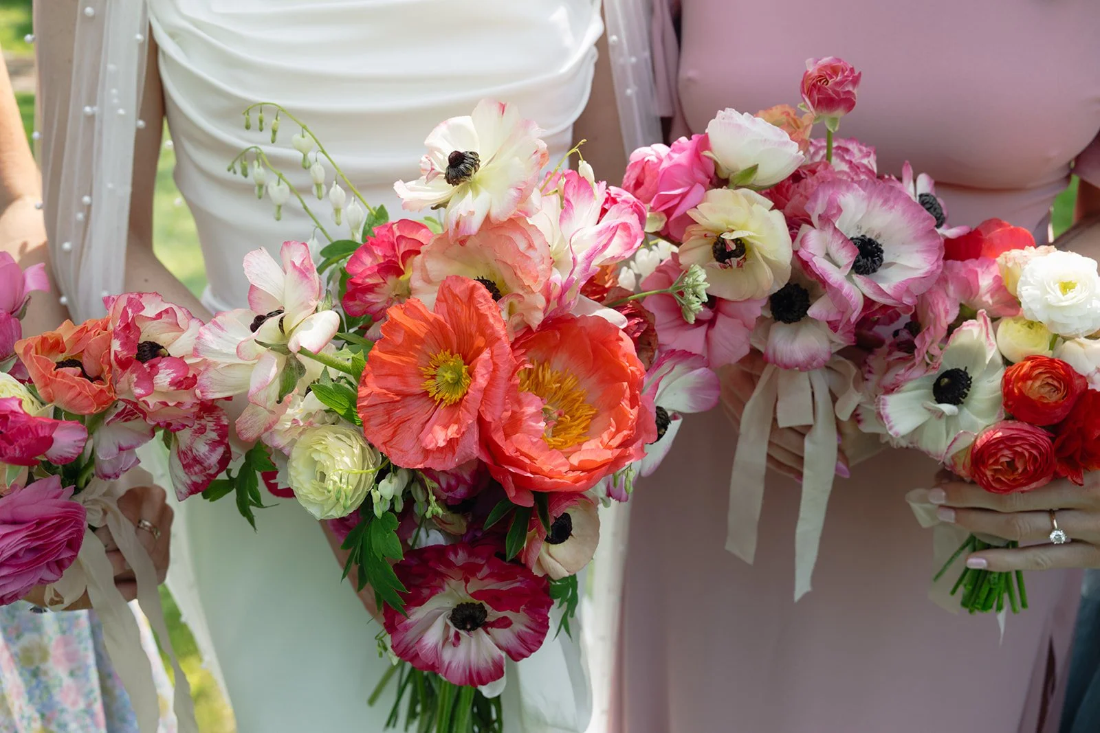 Close-up of several women holding colorful bouquets of pink, white, and orange flowers, including poppies and ranunculus, during a wedding at Lambert's Cove Inn on Martha's Vineyard.