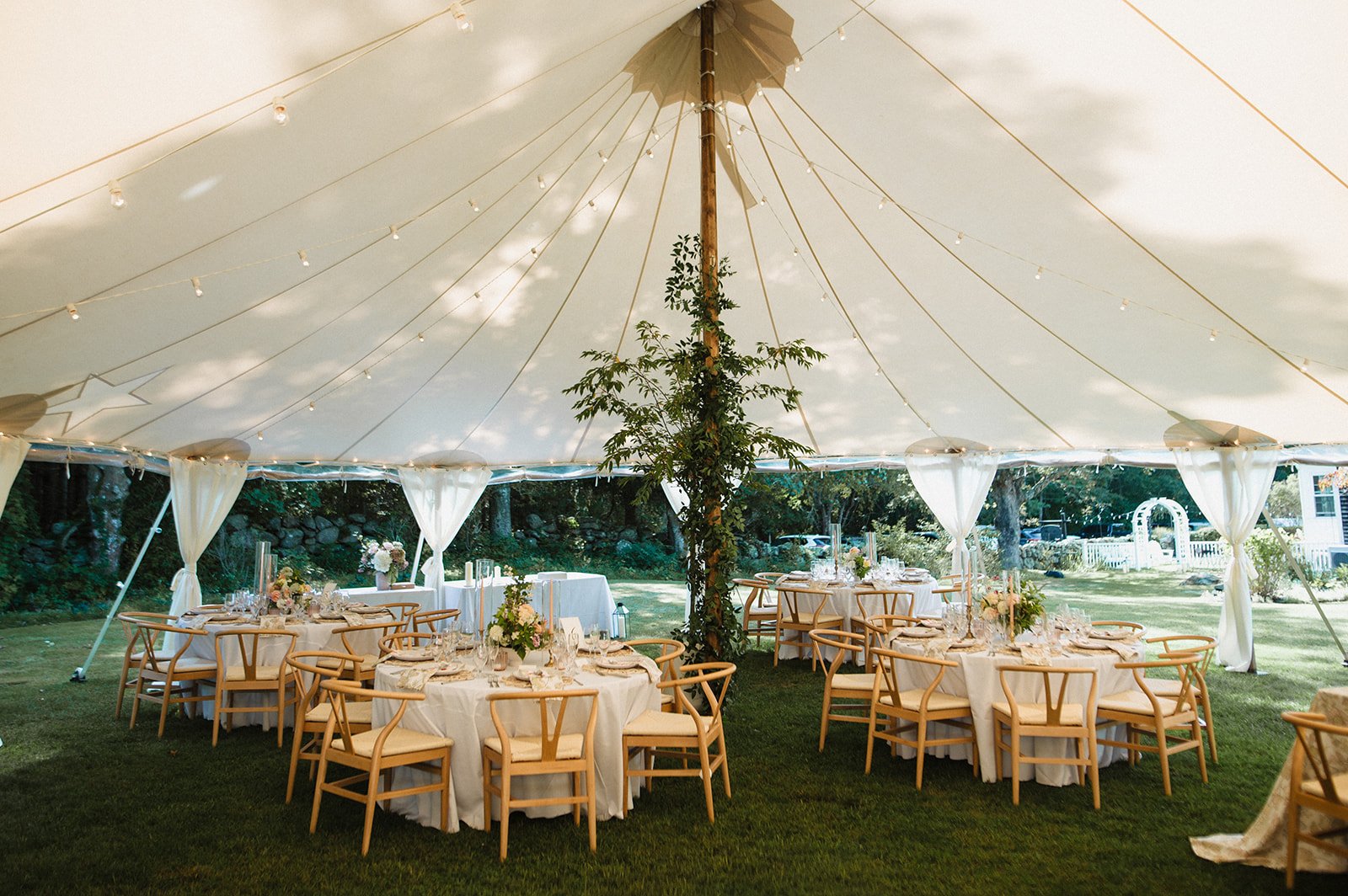 Wedding reception under a large white tent with round tables, wooden chairs, and floral centerpieces on a grassy outdoor area at Lambert's Cove Inn on Martha's Vineyard.