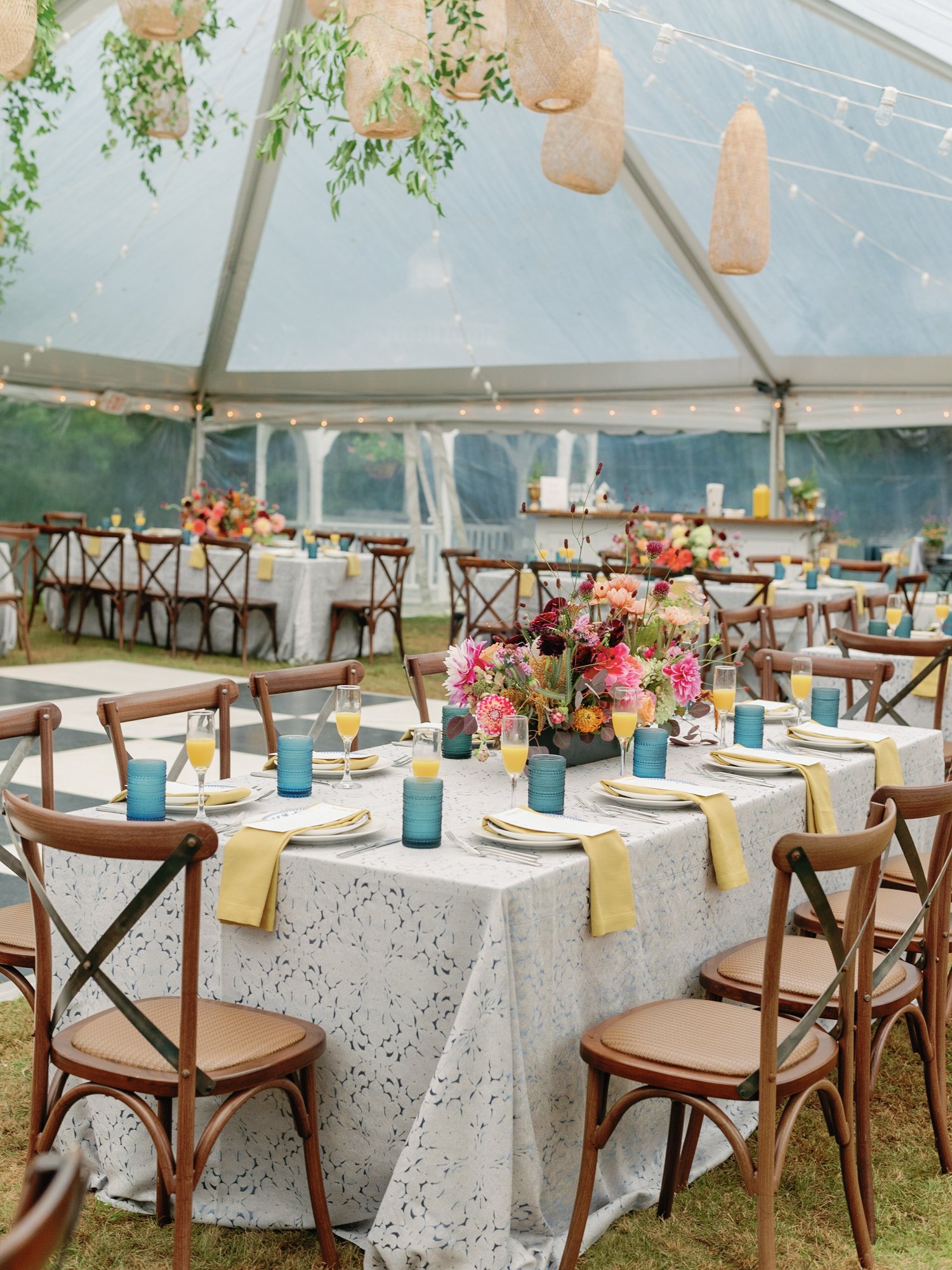 Decorated outdoor wedding reception area under a tent at Lambert's Cove Inn on Martha's Vineyard with round tables covered in white lace tablecloths, floral centerpieces, and yellow napkins.