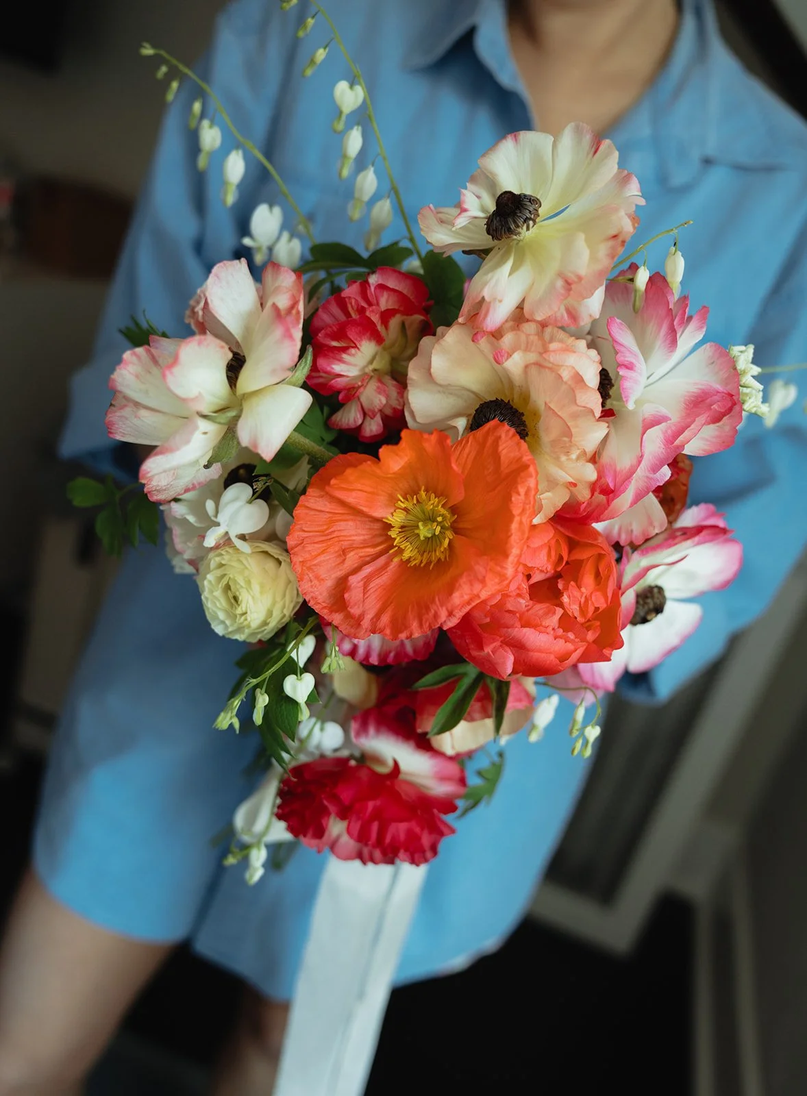 Person holding a mixed bouquet of colorful flowers including poppies and other blooms.