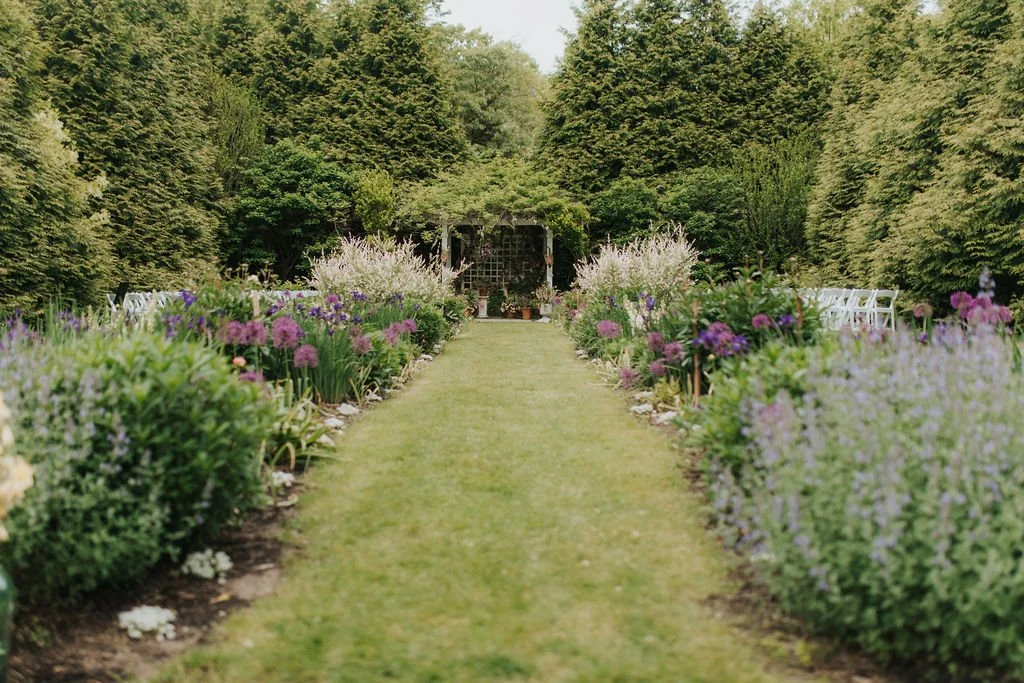 A garden pathway at Lambert's Cove Inn on Martha's Vineyard lined with colorful flowers and greenery leading to a garden shed in the background.