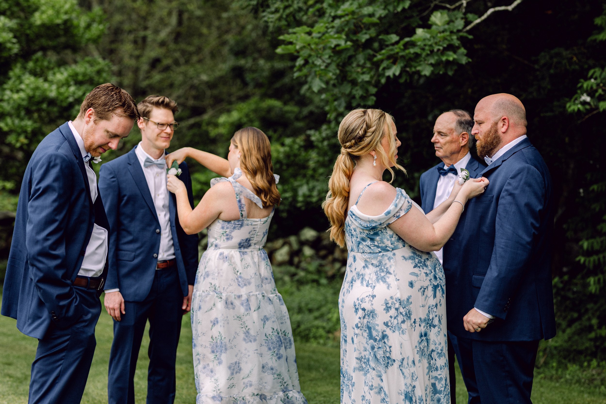 Group of people dressed in formal attire, participating in a wedding ceremony outdoors at Lambert's Cove Inn on Martha's Vineyard surrounded by greenery.