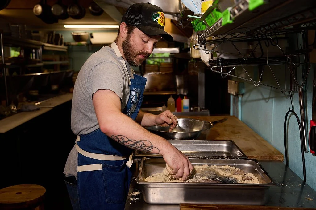 Man coating fish fillets with breading in a kitchen.