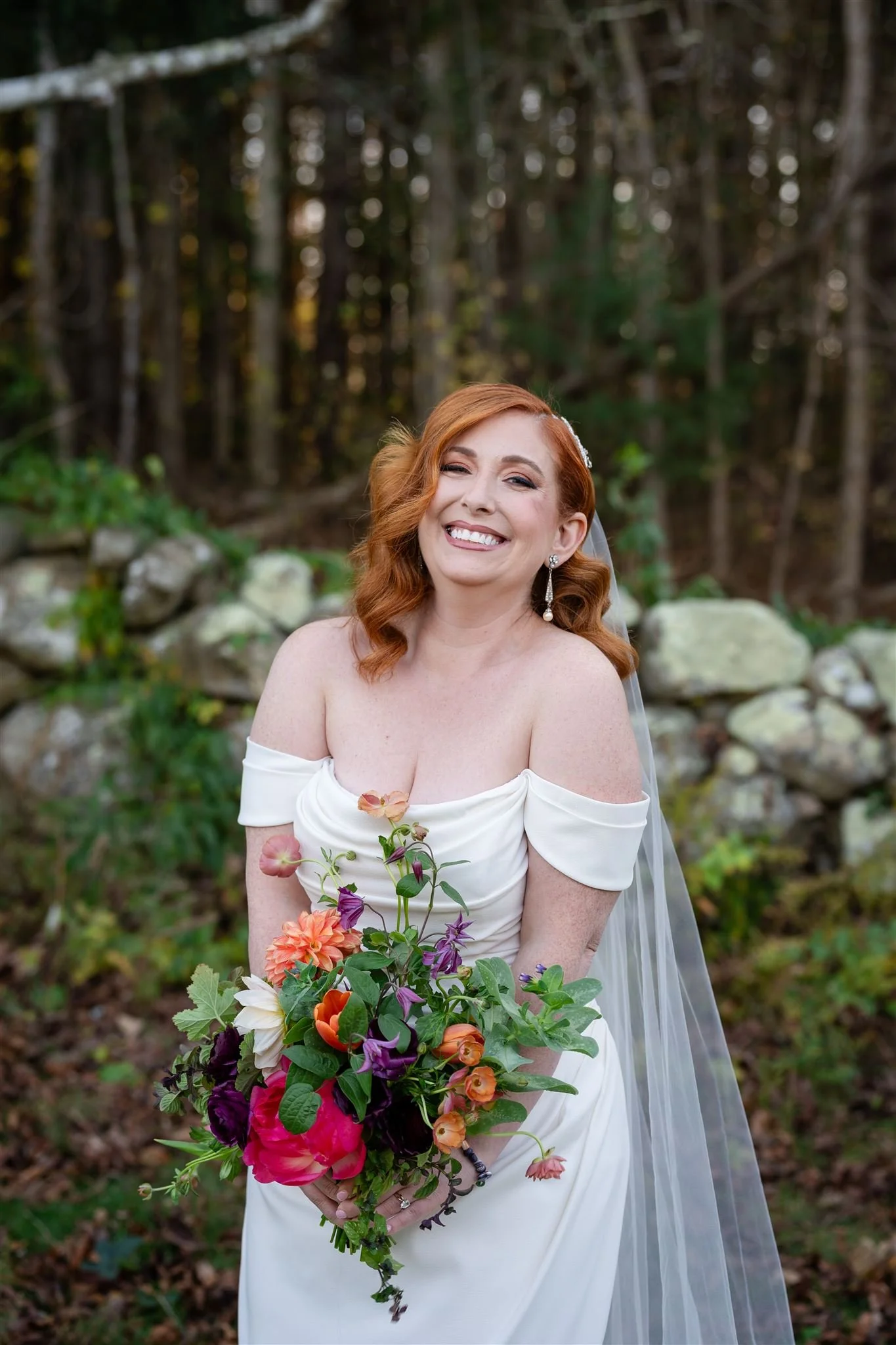 A bride with red hair in a wedding dress holding a bouquet of colorful flowers outdoors at Lambert's Cove Inn on Martha's Vineyard.