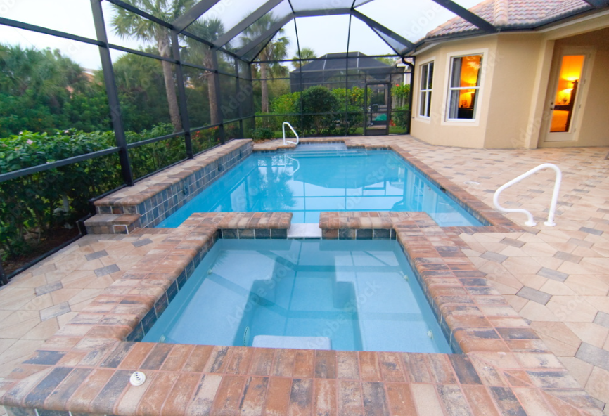 Enclosed backyard swimming pool with a hot tub, brick edging, and a screened enclosure, adjacent to a house with lit windows.