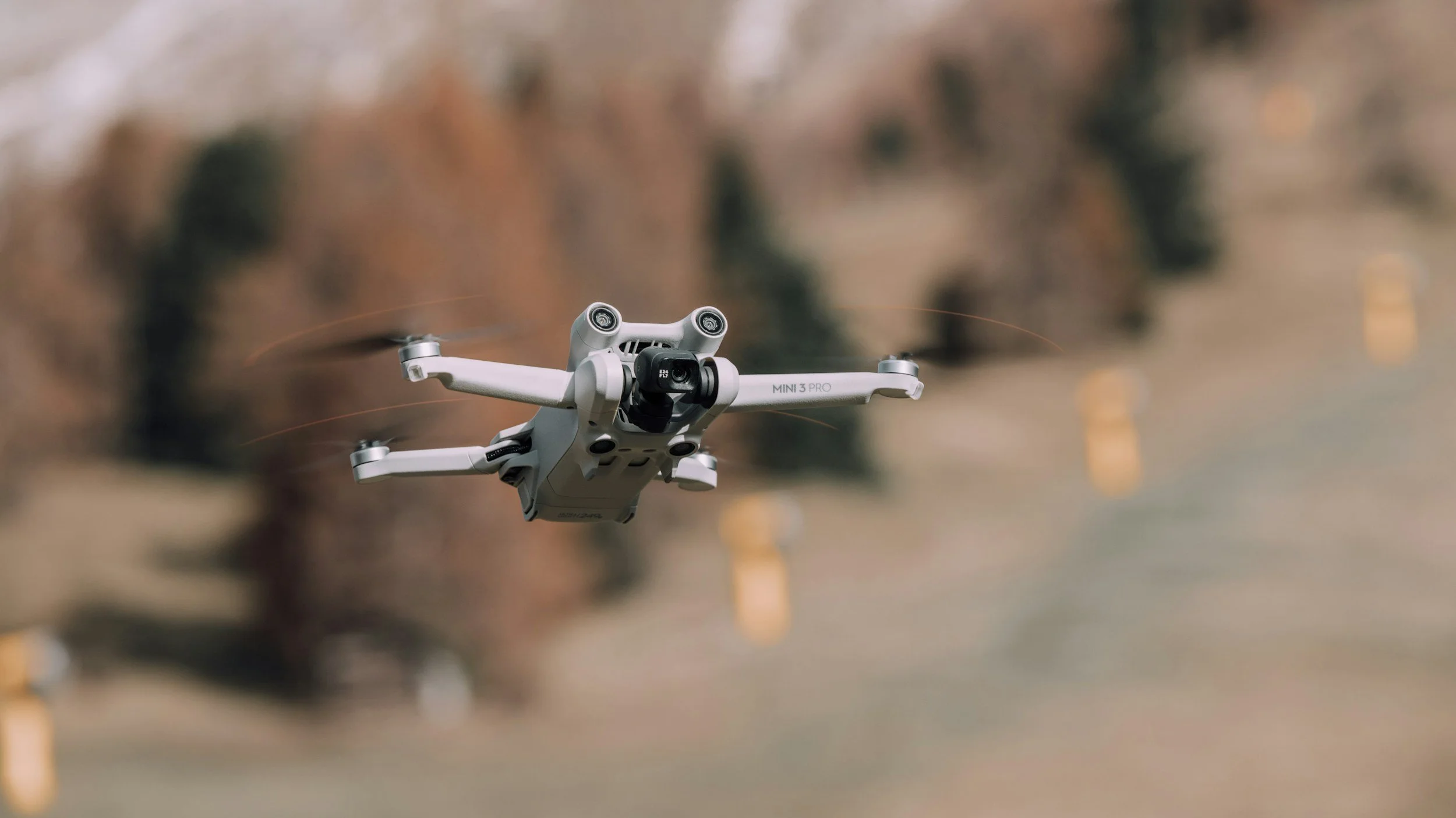 A drone flying outdoors during daytime with blurred background of trees and a field.