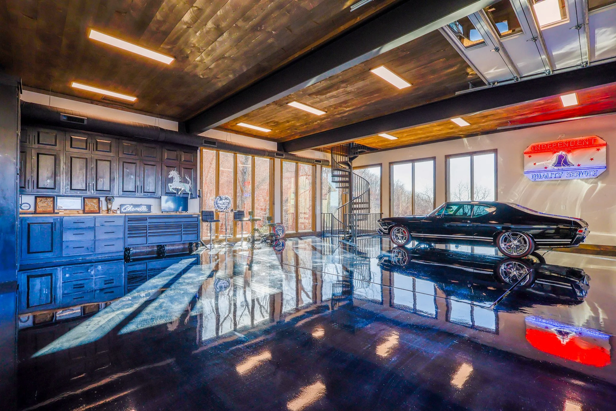 Interior of a modern garage with a classic black car, wooden ceiling, large windows, neon sign, and industrial-style decor.
