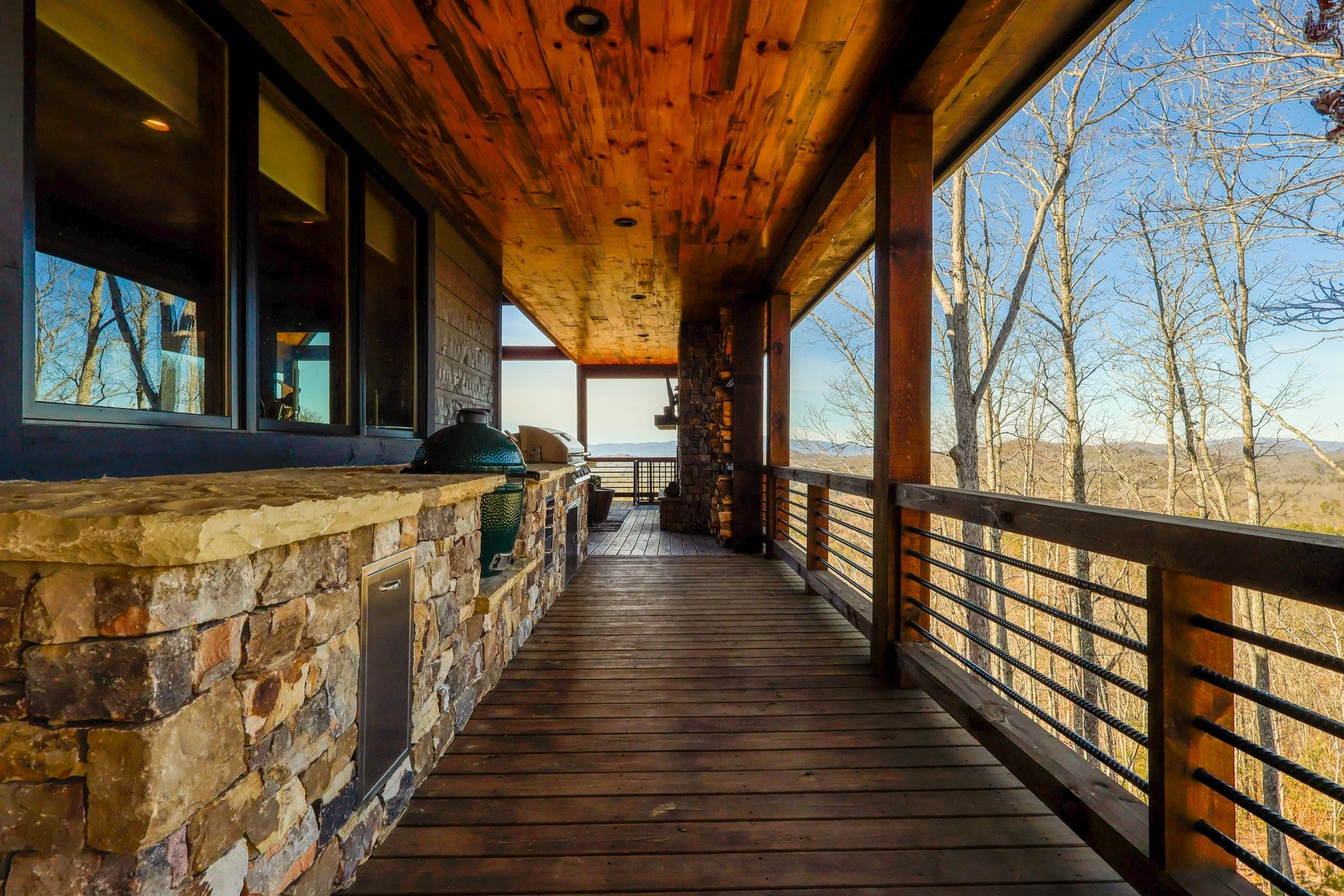 Covered outdoor balcony with a stone and wood counter, a barbecue grill, and a view of leafless trees and distant hills.