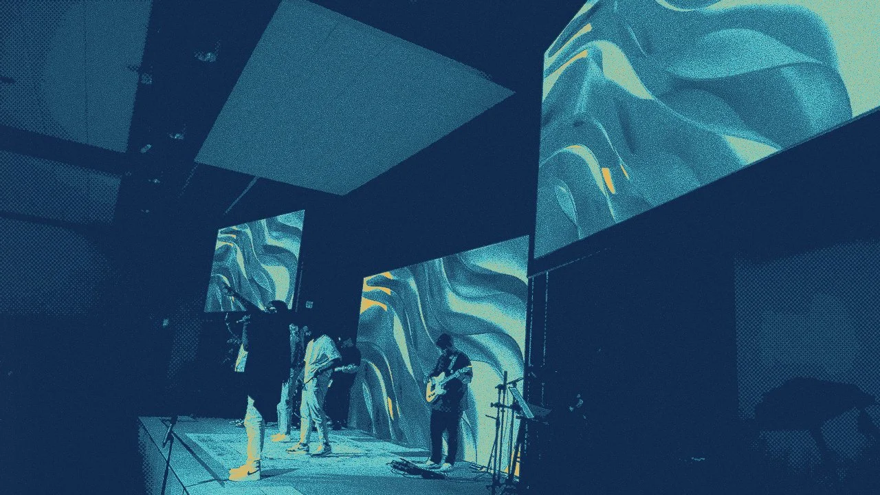 A band performing on a stage with large screens displaying abstract visuals in the background.