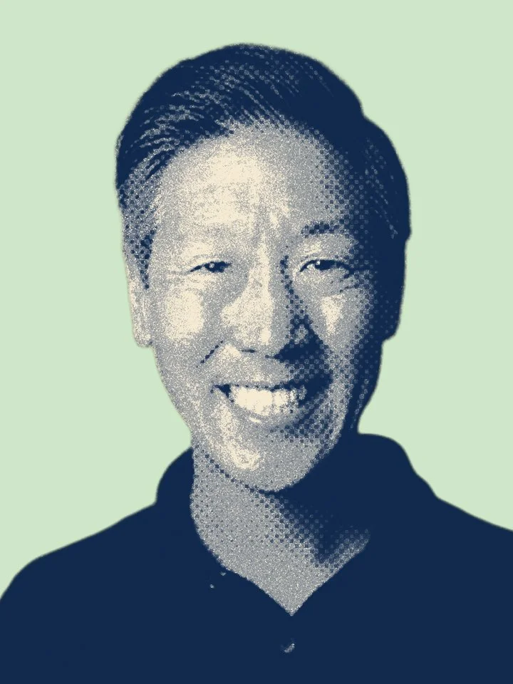 A smiling person with short hair wearing a dark top against a light green background.