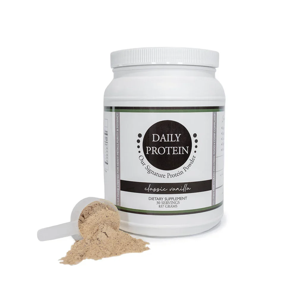 Container of Daily Protein powder with vanilla flavor, scoop of powder, and some powder spilled next to it.