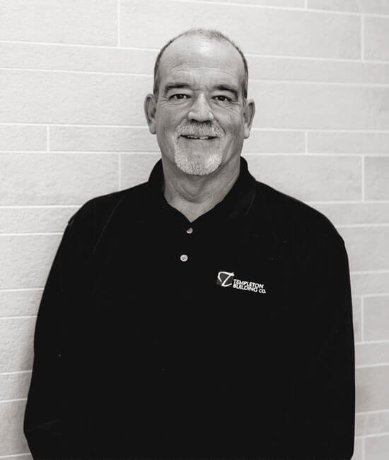 A man with short hair, a beard, and mustache, wearing a black polo shirt with the logo 'Templeton Building Co.' standing in front of a light-colored brick wall.