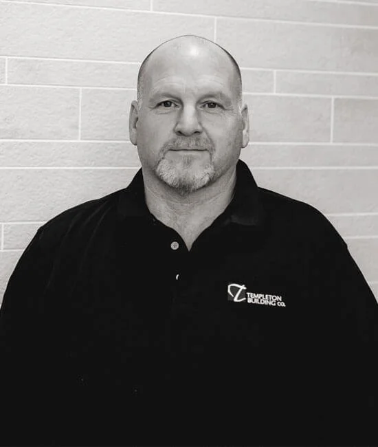 A bald man with a goatee, wearing a black polo shirt with a logo that reads 'Templeton Building Co.' standing against a tiled wall.