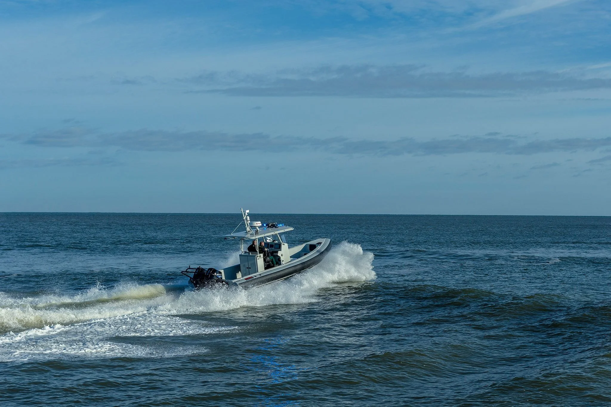A motorboat speeding across the ocean, creating waves and spray, with a cloudy sky in the background.